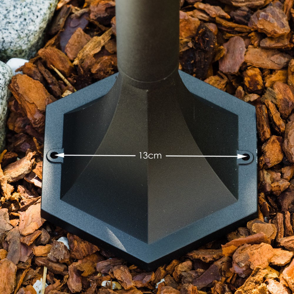 Schwarze, sechseckige Basis einer Lampe mit einer Messung von 13 cm. Sie ruht auf braunem Mulch. Der Pfahl der Lampe ist sichtbar.