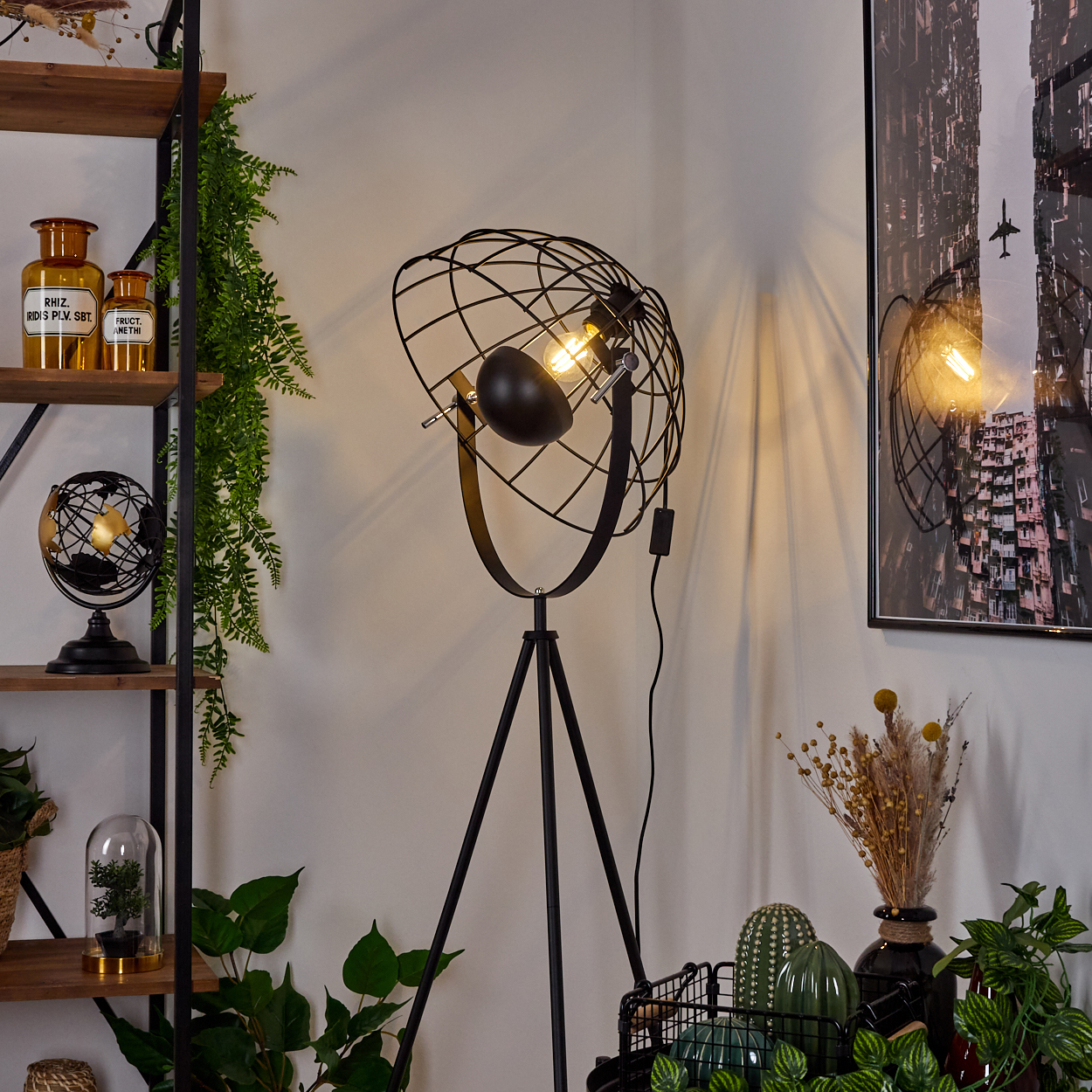 Eine moderne schwarze Stehlampe mit kugelförmigem Käfigschirm ist beleuchtet. Regale mit Dekor und Pflanzen befinden sich links. Rechts ist ein Stadtbild.