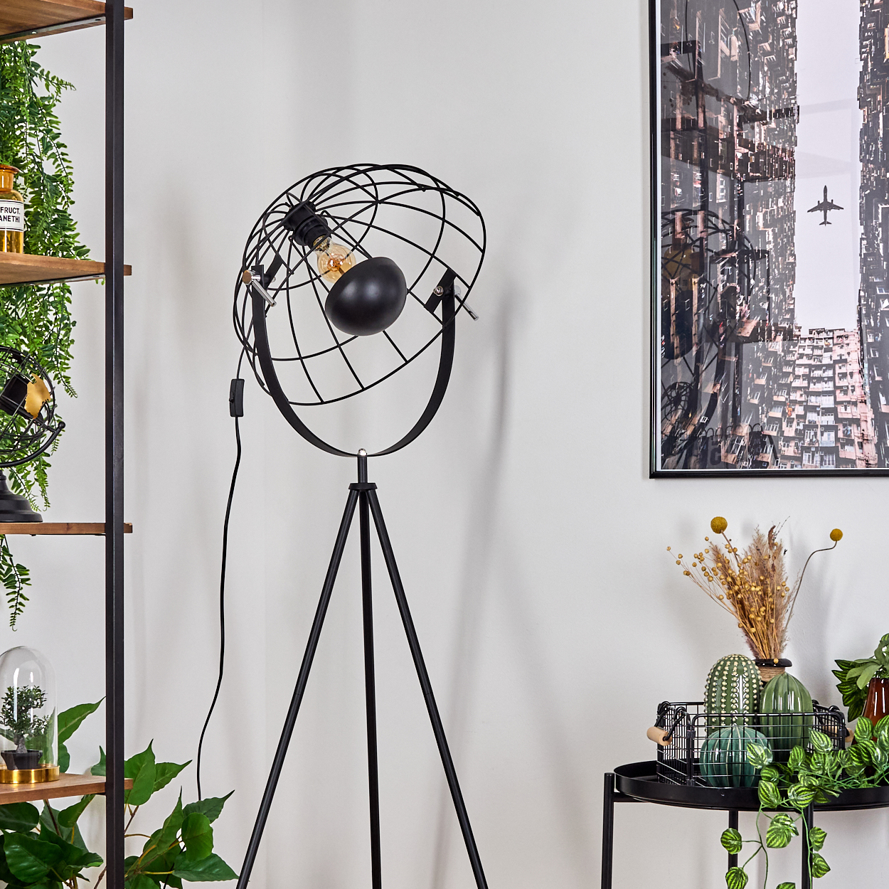 Schwarze Metall-Stehlampe mit kugelförmigem Schirm. Im Hintergrund ein Bild einer Stadt und Pflanzen.
