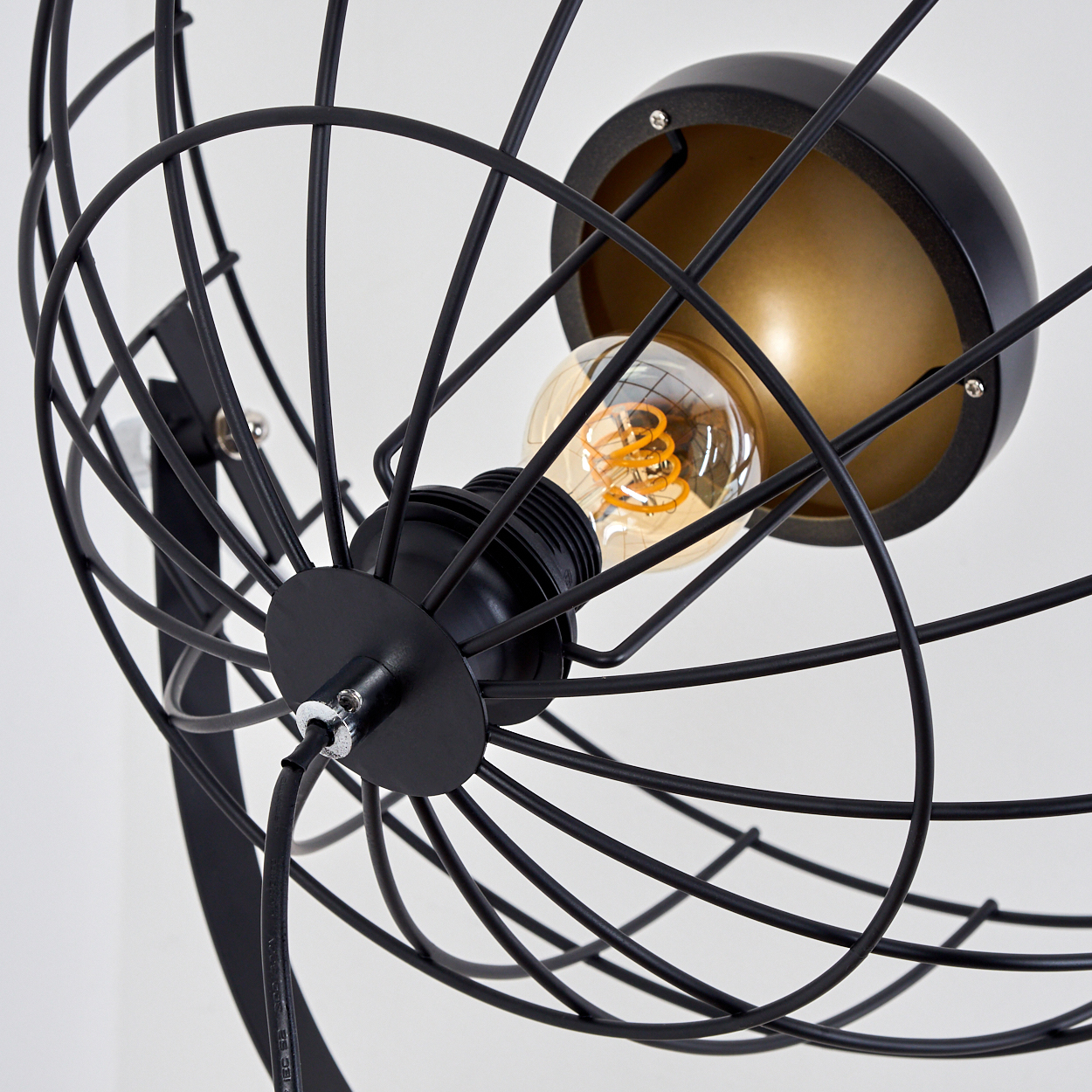 Nahaufnahme einer schwarzen Metalllampe mit käfigartigem Design um eine Glühbirne. Der Hintergrund ist weiß.