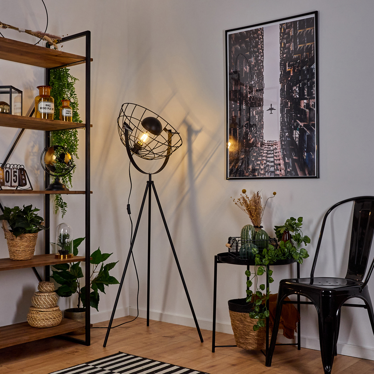 Raumecke mit Stehlampe, Regalen mit Deko, schwarzem Stuhl und Gebäude-Bild. Ein kleiner Tisch hat Pflanzen.