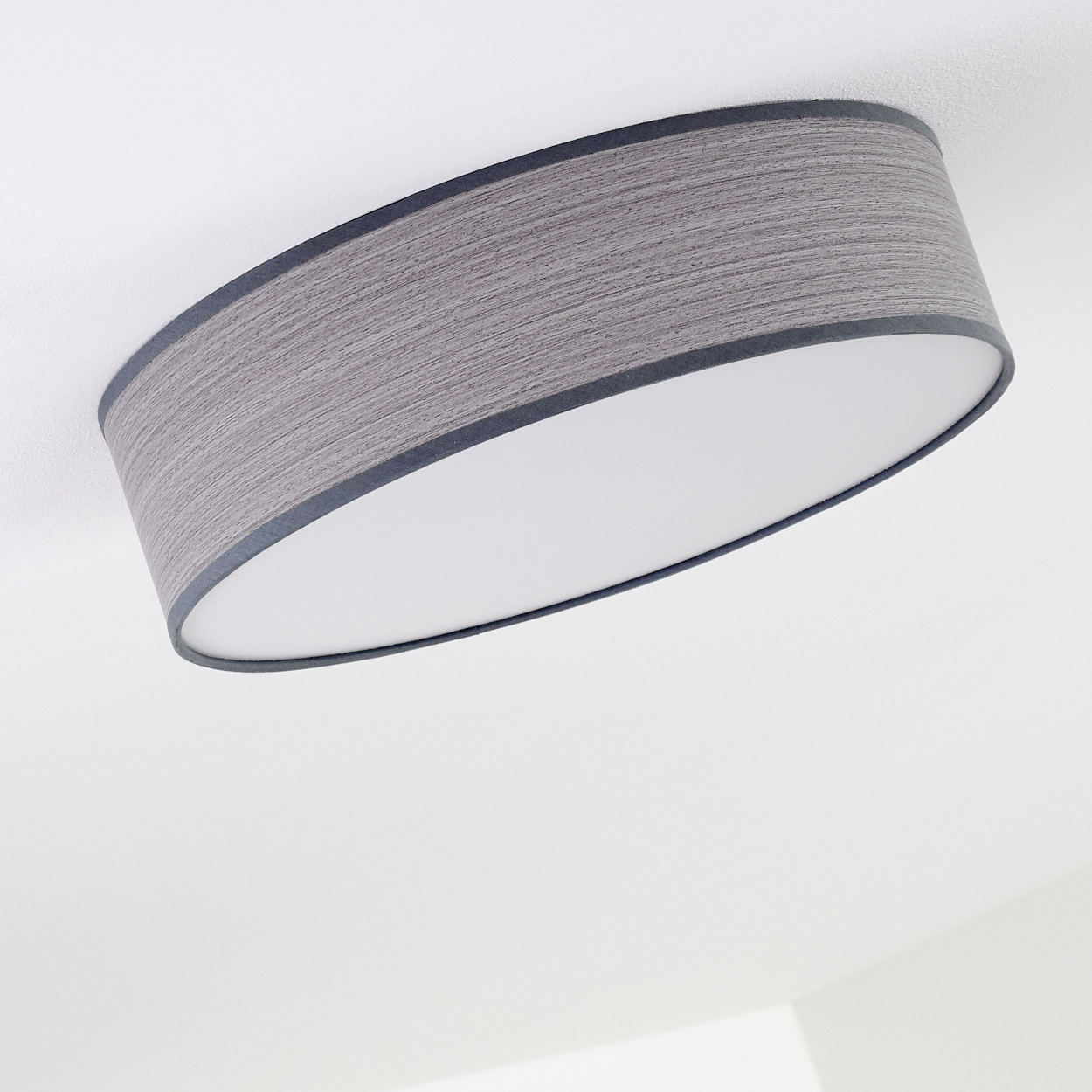 Eine graue, zylindrische Deckenlampe mit weißem Innenraum. Die Lampe hat eine dunkelgraue Umrandung und ist an einer weißen Decke.