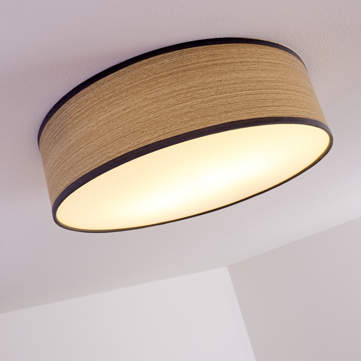 Eine Deckenleuchte mit Holzschirm und dunklem Rand. Das Licht ist an und beleuchtet die weiße Decke und Ecken.
