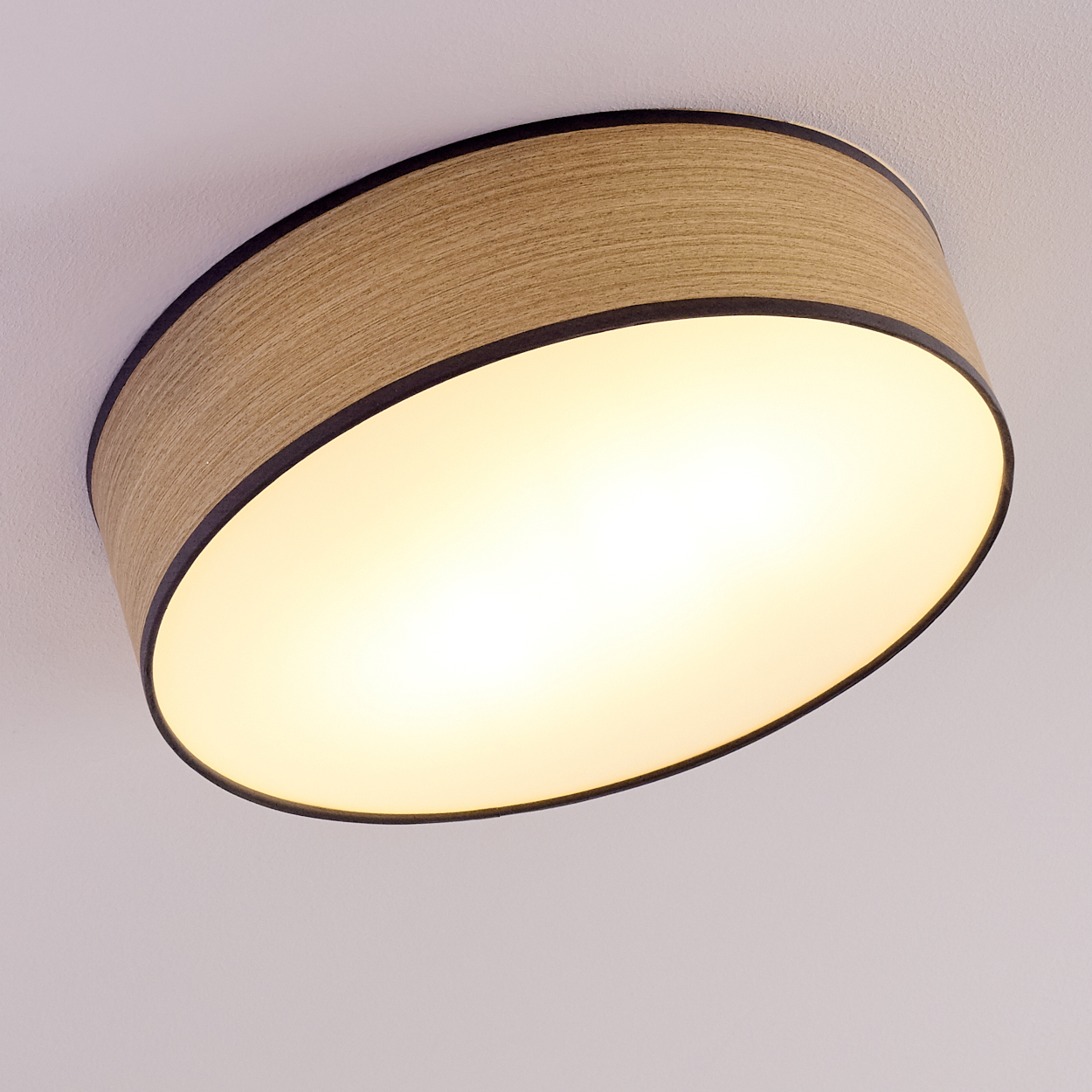 Eine Deckenleuchte mit Holzschirm und schwarzem Rand. Das Licht ist oval und strahlt warmes, gelbes Licht aus.