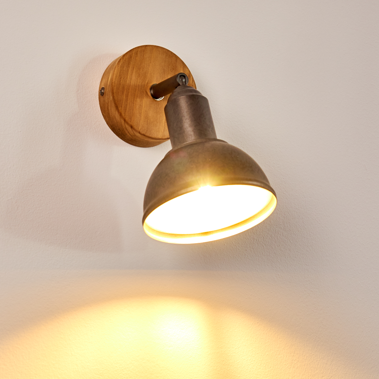 Eine Wandleuchte mit Holzsockel und metallischem Lampenschirm, die ein warmes Licht an die Wand wirft.