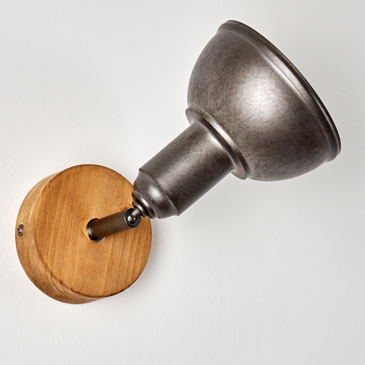Ein Metall-Spotlight ist auf einer Holzbasis montiert, die an einer weißen Wand befestigt ist. Der Scheinwerfer ist abgewinkelt.