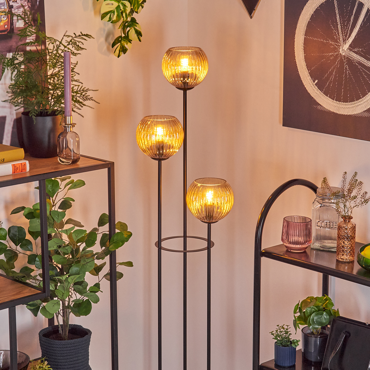 Ein dekorativer Raum mit einer dreifachen Lampe, Pflanzen und Regalen mit verschiedenen Gegenständen, darunter Kerzen und Bücher.