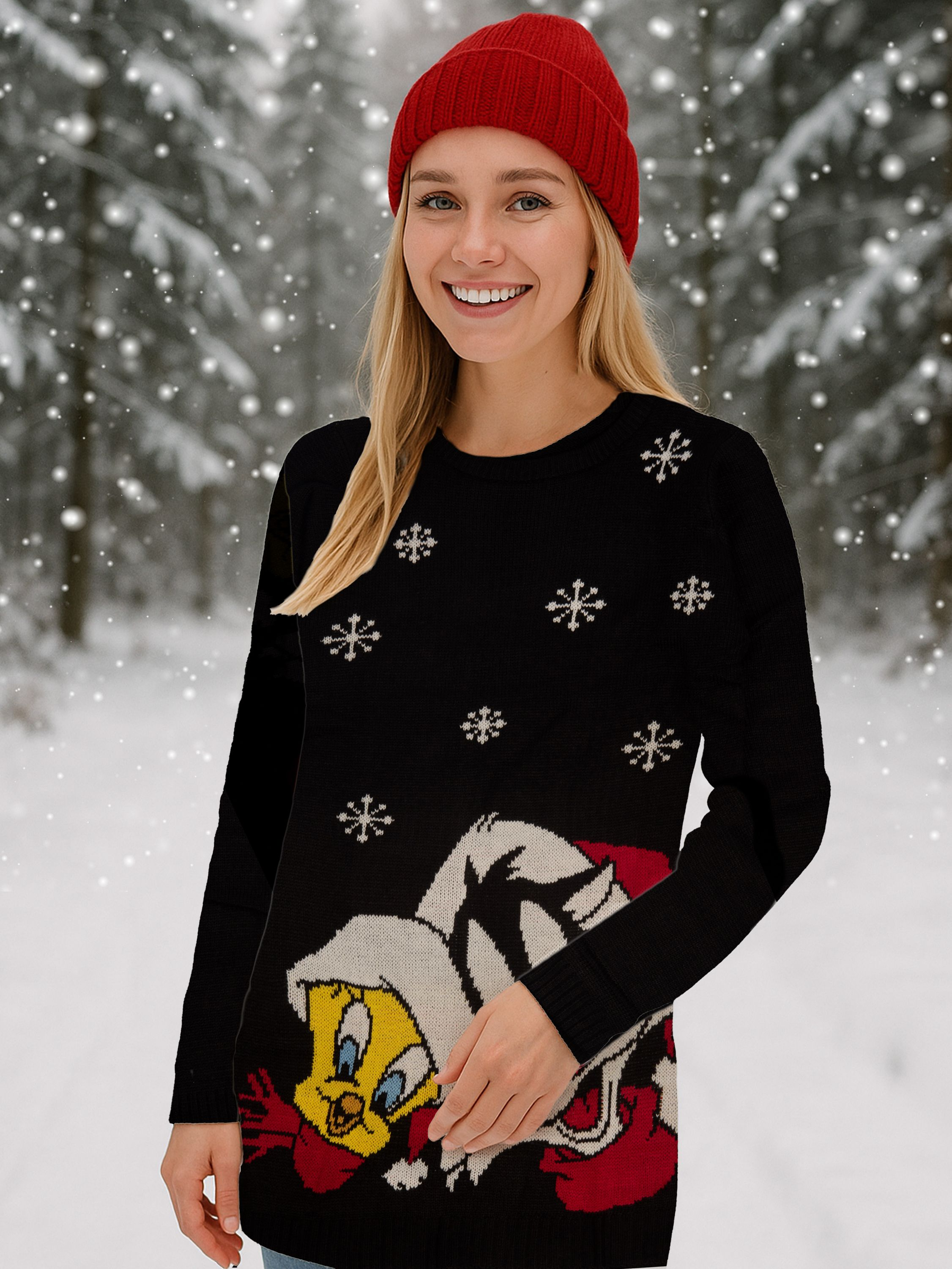 Frau mit roter Mütze und schwarzem Pullover mit Schneeflocken und Tweety Bird-Design, lächelnd, verschneiter Hintergrund.