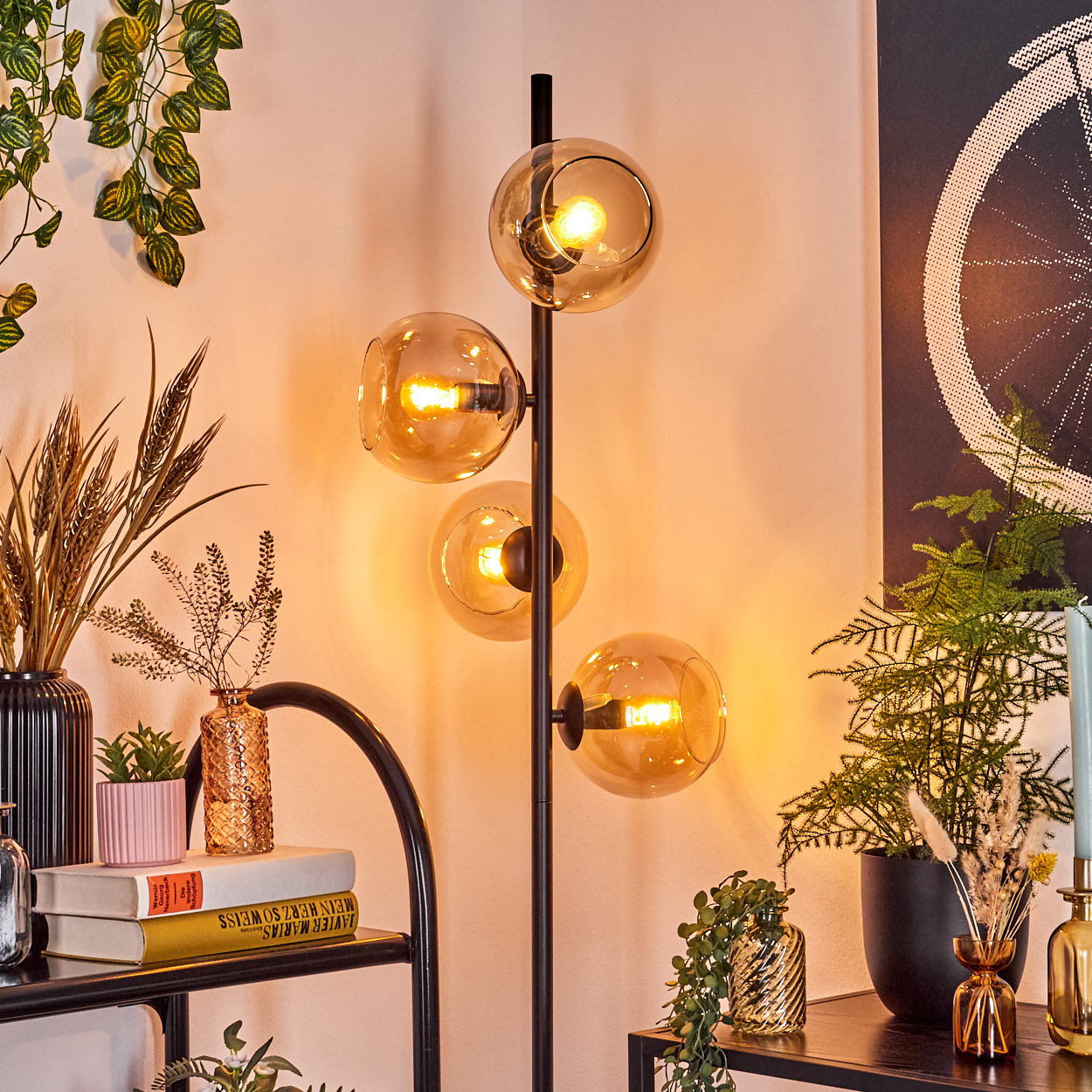 Eine moderne Stehlampe mit vier bernsteinfarbenen Glaskugeln beleuchtet einen Raum mit Pflanzen und Dekorationsartikeln.