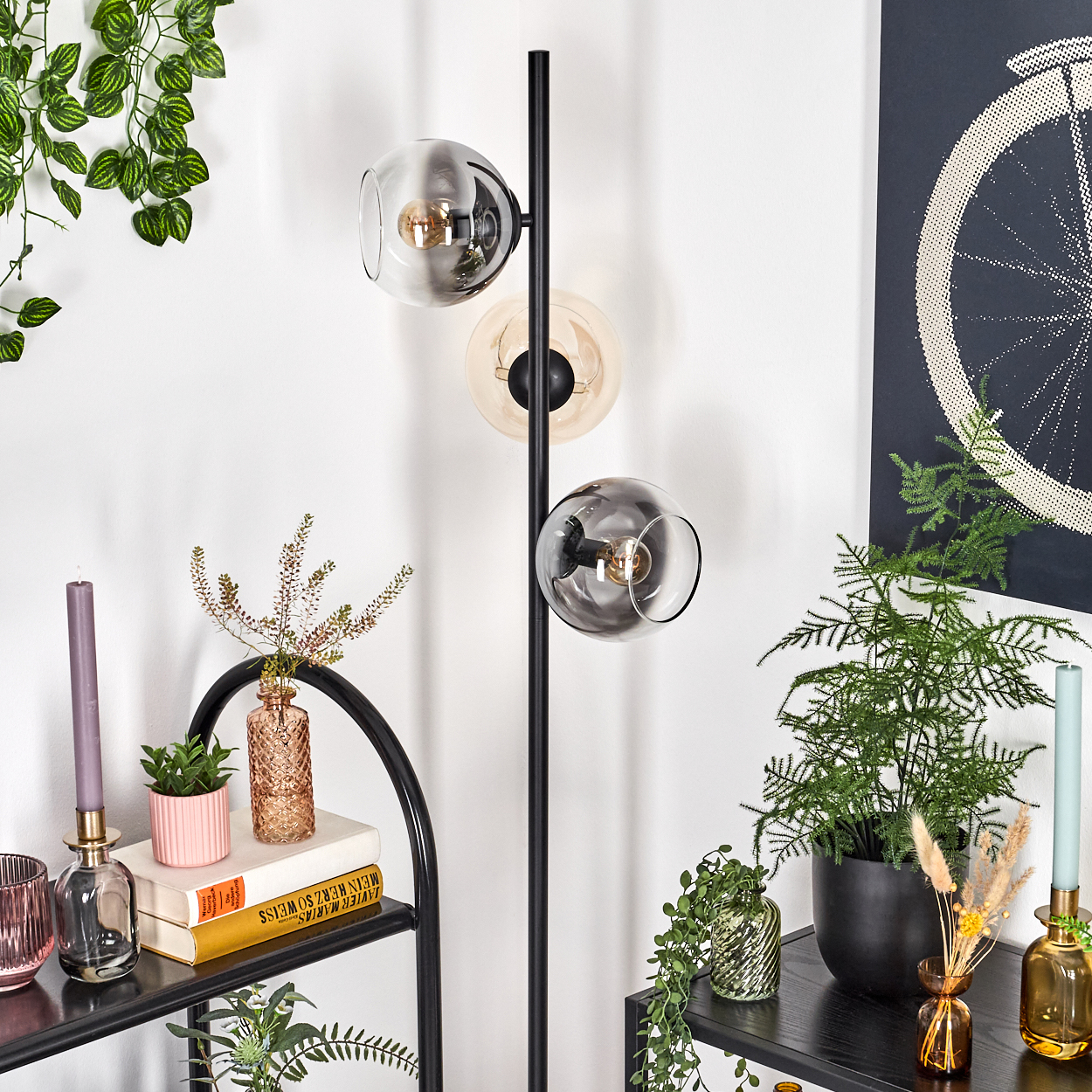 Eine moderne Stehlampe mit Glaskugelschirmen steht in der Nähe von Pflanzen und einem schwarzen Regal und schmückt einen Raum.