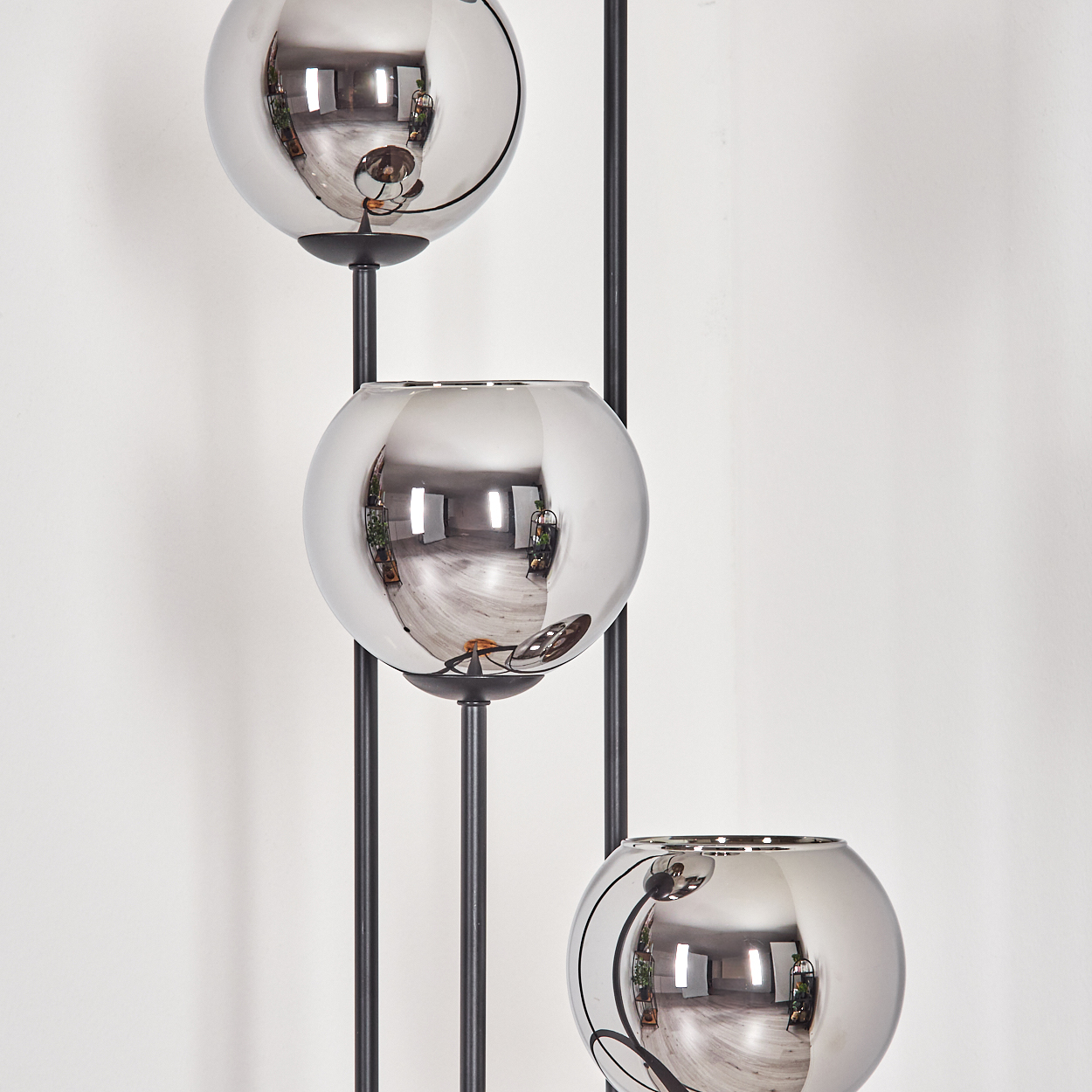 Drei verspiegelte Kugeln auf schwarzen Stützen vor einer weißen Wand. Die Kugeln reflektieren einen Raum mit Fenstern und Pflanzen.
