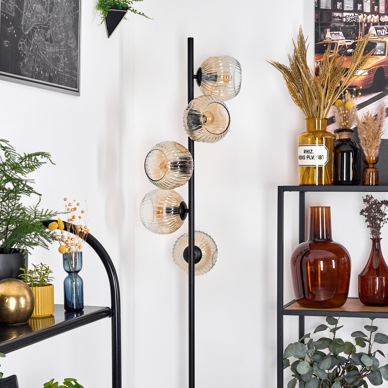 Ein modernes Interieur mit einer schwarzen Lampe mit Glaskugeln. Regale halten Vasen, Pflanzen und ein Kartenbild. Weißer Wandhintergrund.