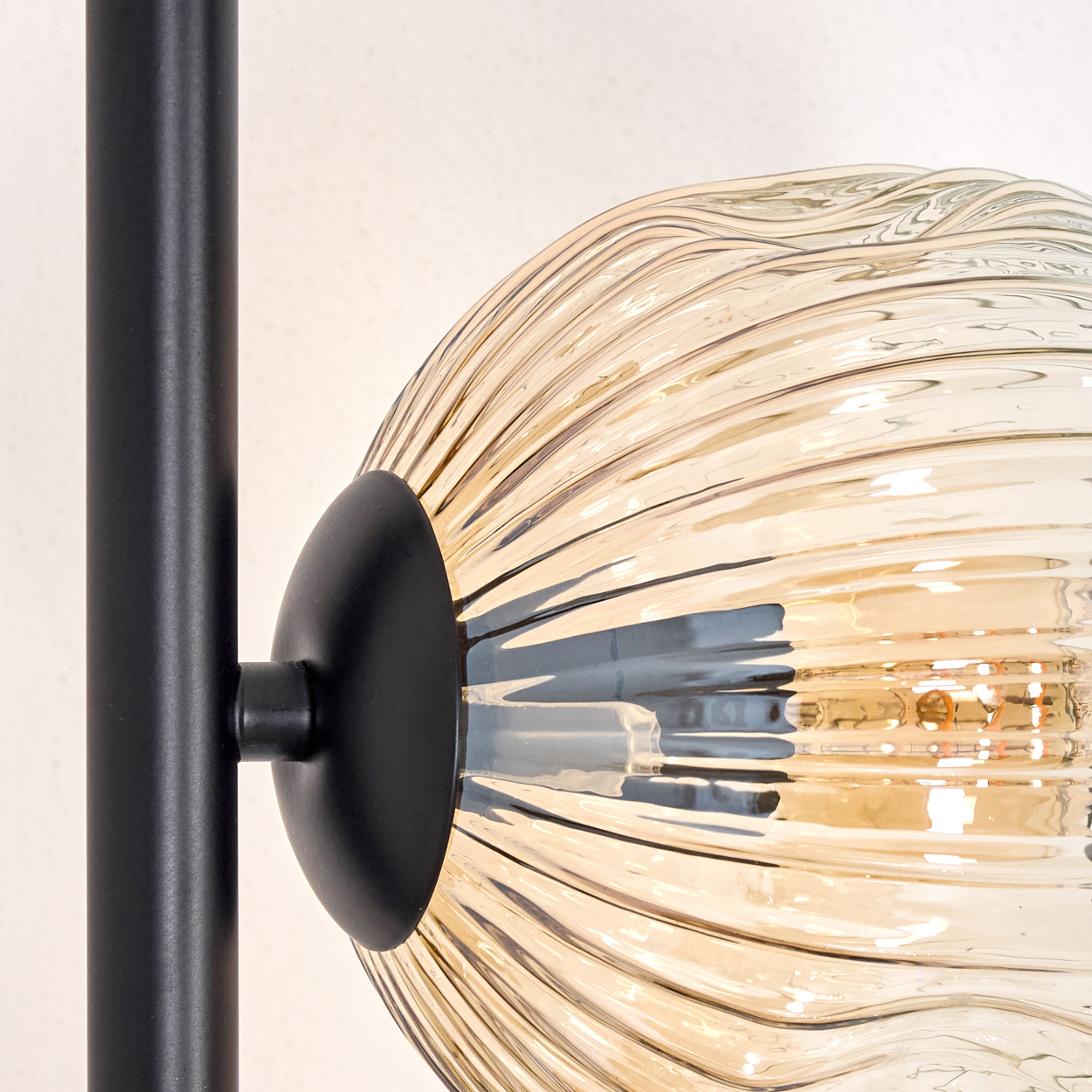 Nahaufnahme einer Lampe mit schwarzem Stiel und einem kugelförmigen, bernsteinfarbenen Glasschirm. Der Schirm hat eine gerippte Textur.
