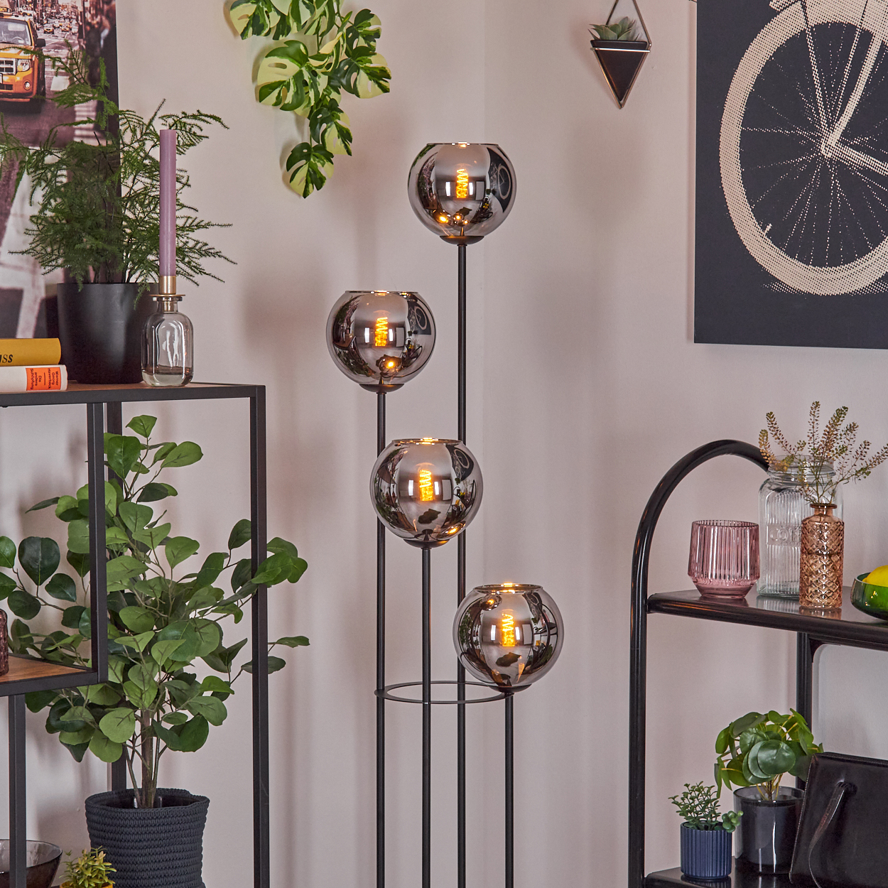 Ein modernes Wohnzimmer mit einer einzigartigen Lampe, Pflanzen und Dekorationsartikeln. Die Lampe hat vier Glaskugeln mit leuchtenden Glühbirnen.