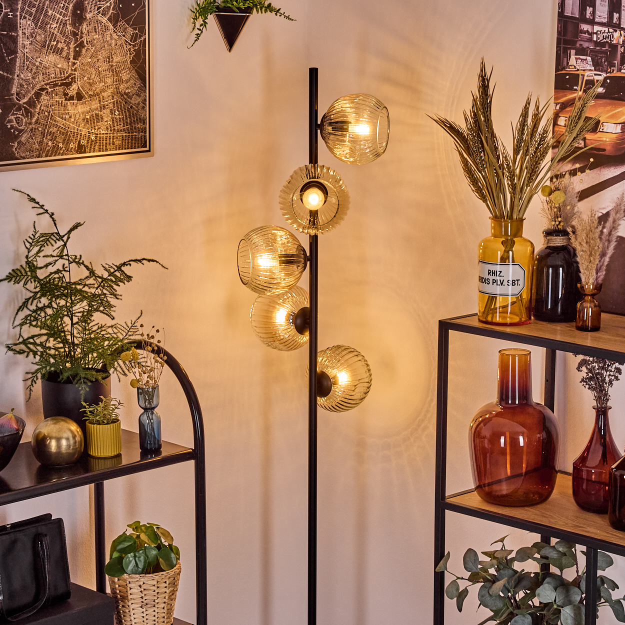 Eine moderne Wohnzimmerecke. Eine hohe Lampe mit Glaskugeln, Regale mit Vasen und Pflanzen sowie eine Karte und ein Poster an der Wand.