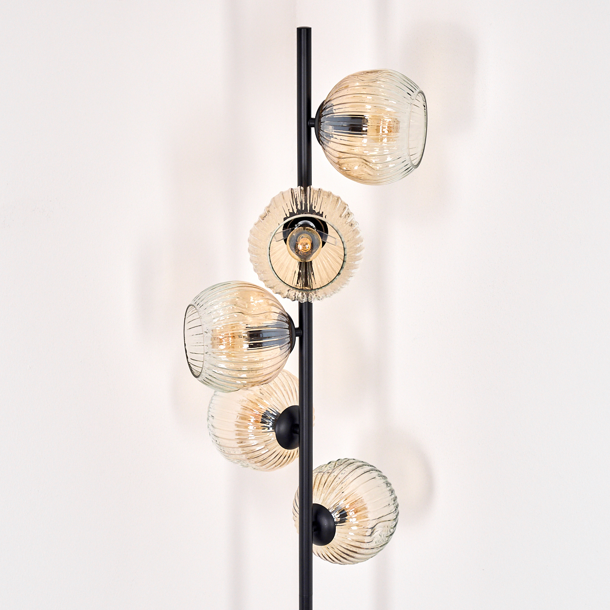 Eine moderne Stehlampe mit fünf Glaskugeln. Die Kugeln sind bernsteinfarben und gerippt. Die Lampe steht vor einer weißen Wand.