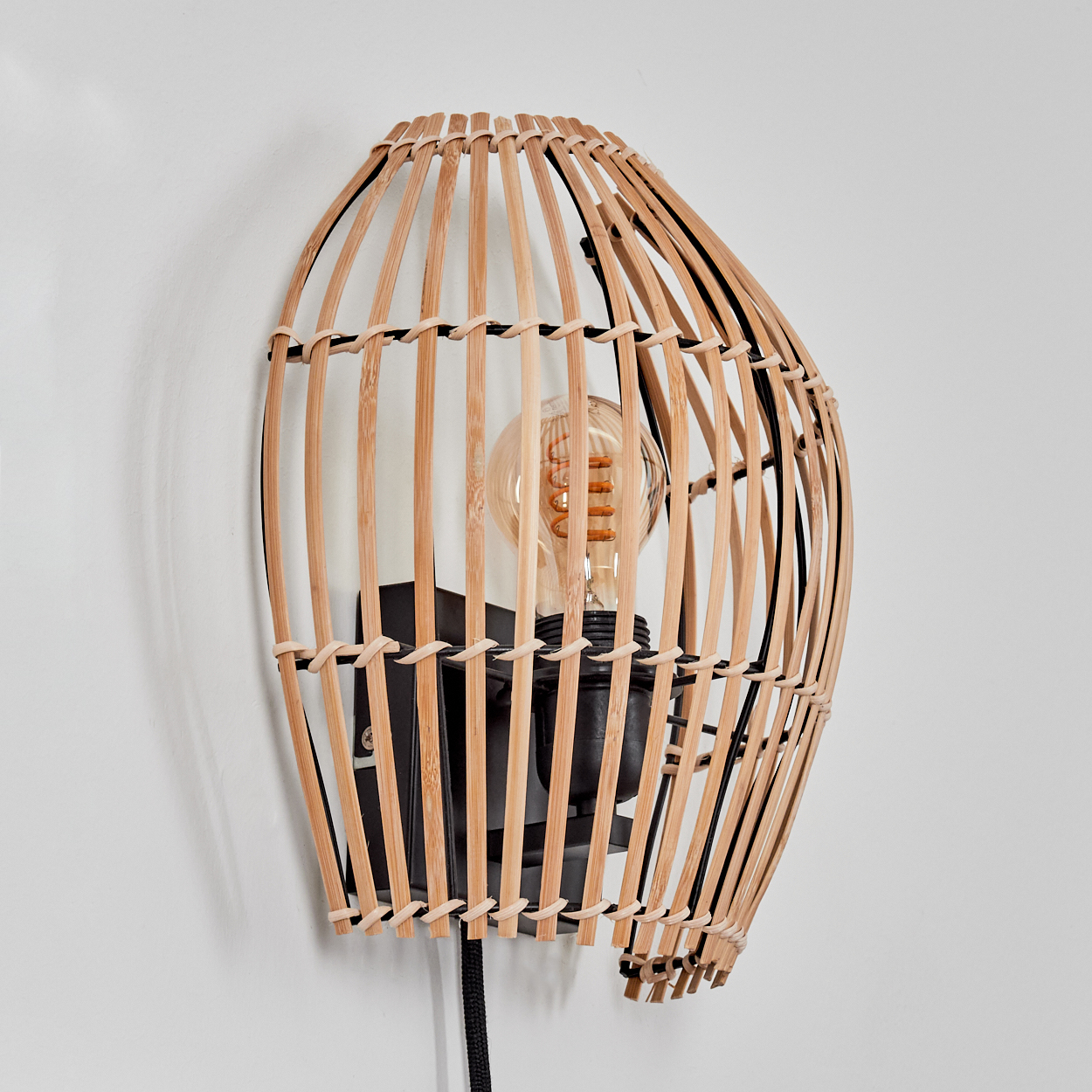 Eine Wandlampe mit einem hölzernen Käfig um eine Glühbirne. Die Lampe ist an einer weißen Wand befestigt.
