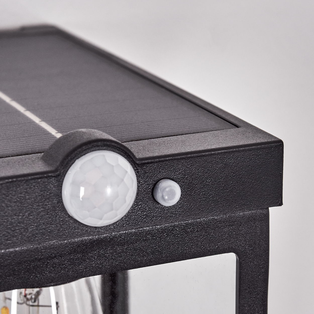 Nahaufnahme einer schwarzen Solarleuchte. Sie hat ein Solarpanel, einen Bewegungssensor und einen kleinen Knopf. Der Hintergrund ist weiß.
