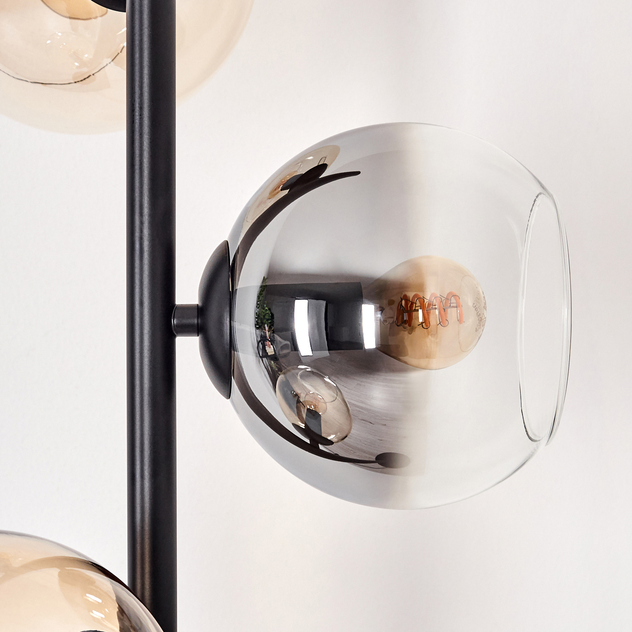 Nahaufnahme einer modernen Lampe. Sie hat drei Glaskugeln, einen schwarzen Metallrahmen und eine sichtbare Glühbirne.