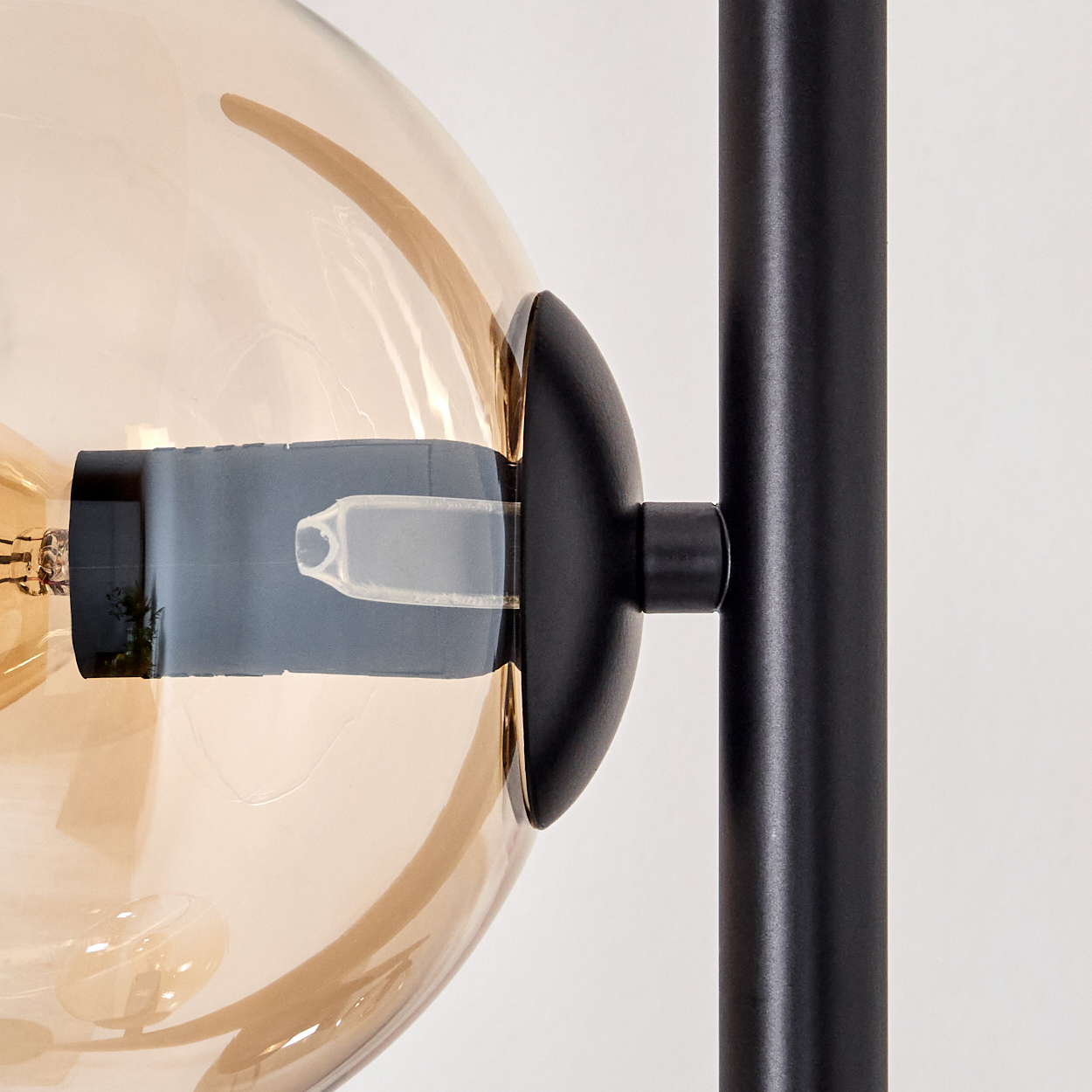 Nahaufnahme einer Lampe. Eine transparente, bernsteinfarbene Glaskugel, eine schwarze Metallhalterung und ein schwarzer Pfosten sind zu sehen.