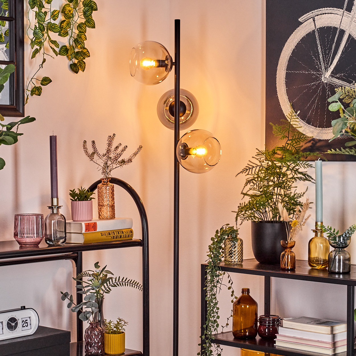 Ein Raum mit einer modernen Stehlampe, Regalen mit Pflanzen, Vasen, Büchern und einem Fahrradposter an der Wand.