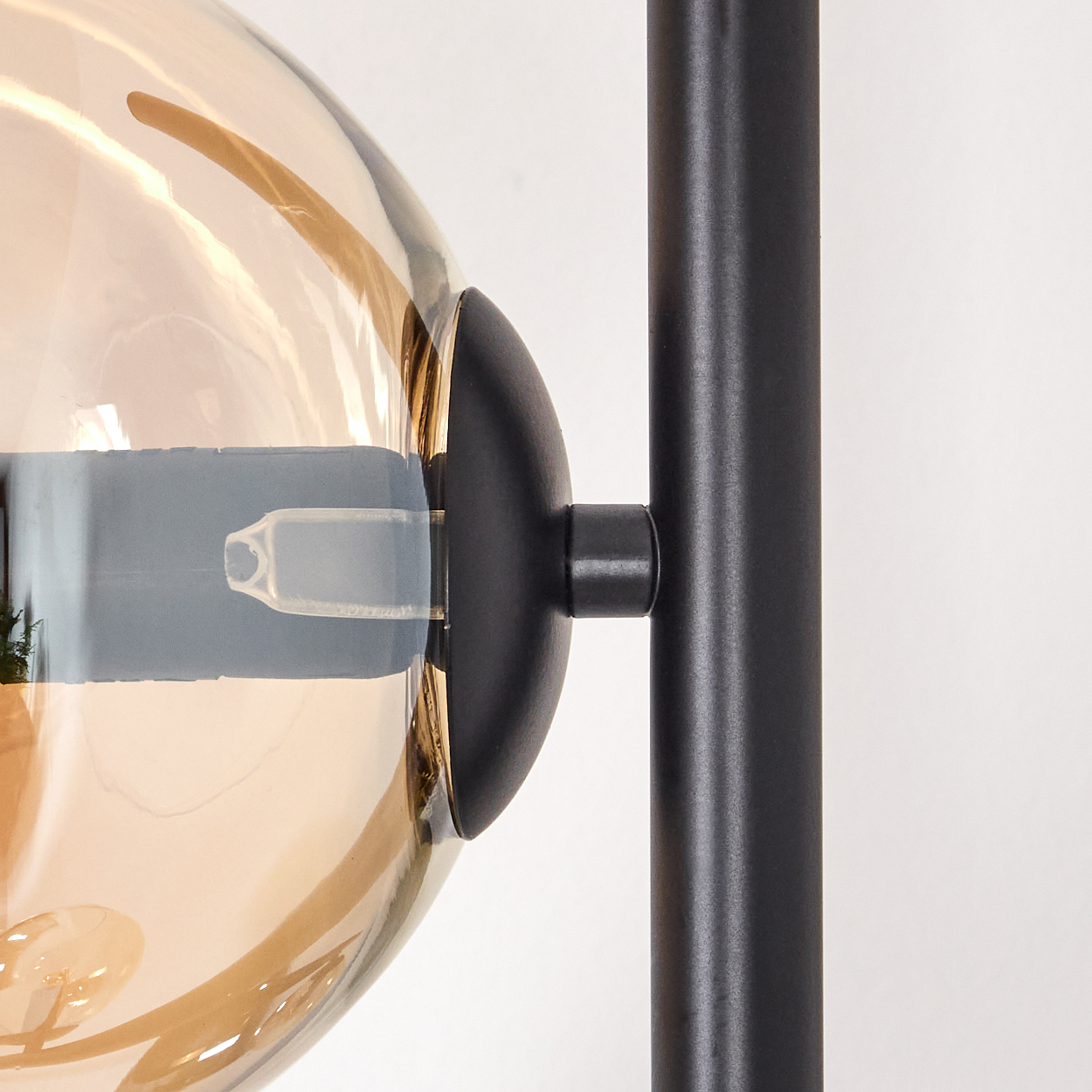 Nahaufnahme einer Lampe. Ein klarer, kugelförmiger, bernsteinfarbener Glasschirm neben einer schwarzen Metallstange.