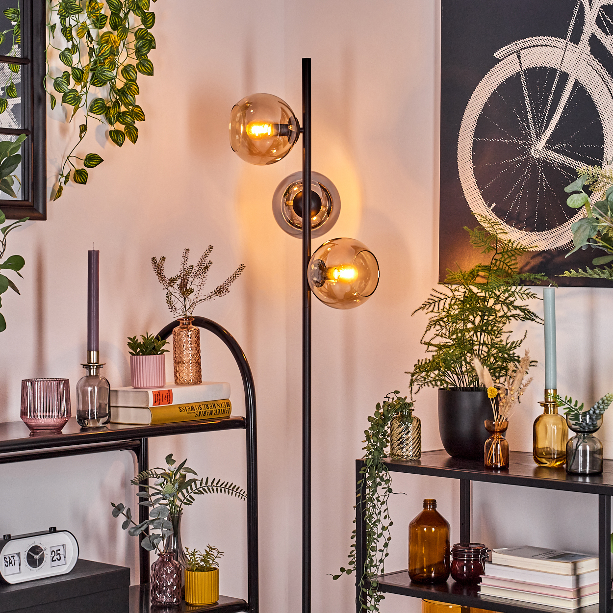 Raumecke mit Stehlampe. Regale mit Pflanzen, Büchern und Deko. Fahrradrad-Kunstwerk an der Wand.