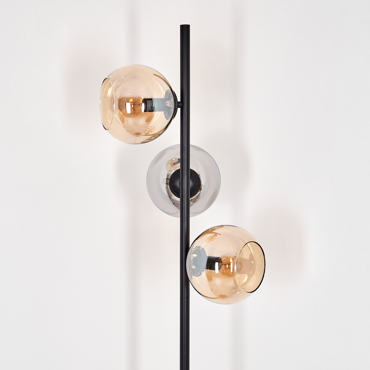 Eine moderne Stehlampe mit drei Glaskugelschirmen. Die Schirme sind bernsteinfarben und klar, mit schwarzem Metall an weißer Wand.