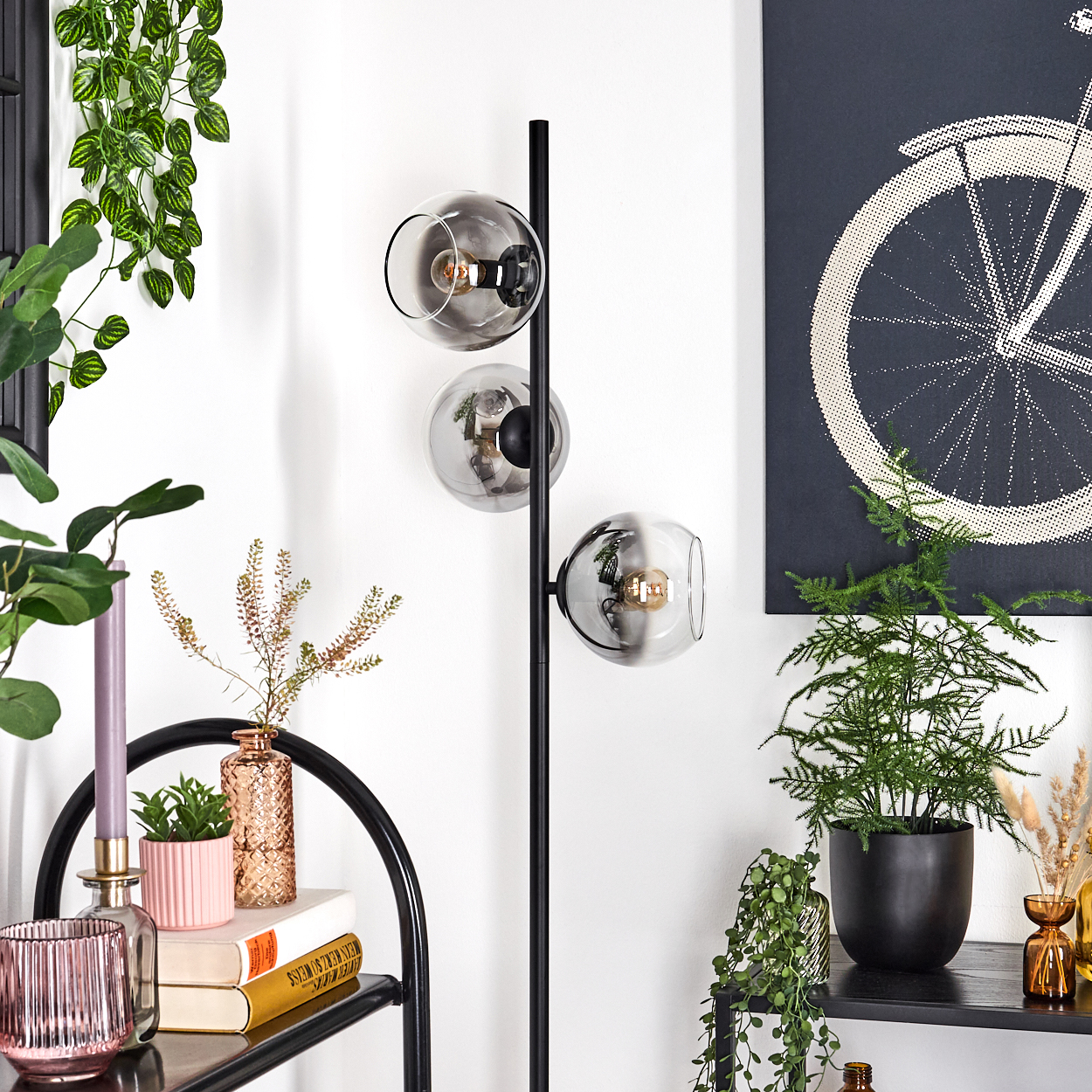 Ein modernes Zimmer mit einer schwarzen Stehlampe mit drei Glaskugeln. An der Wand befindet sich ein Bild eines Fahrradrads.
