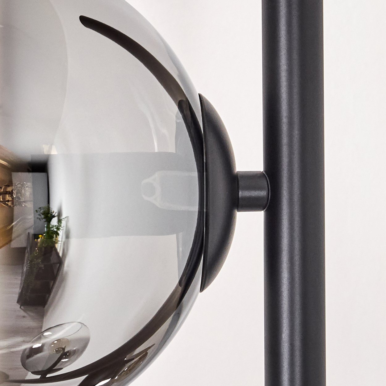 Nahaufnahme einer modernen Lampe. Eine graue Glaskugel ist mit einer schwarzen Metallstange verbunden. Die Reflexion zeigt einen Raum.
