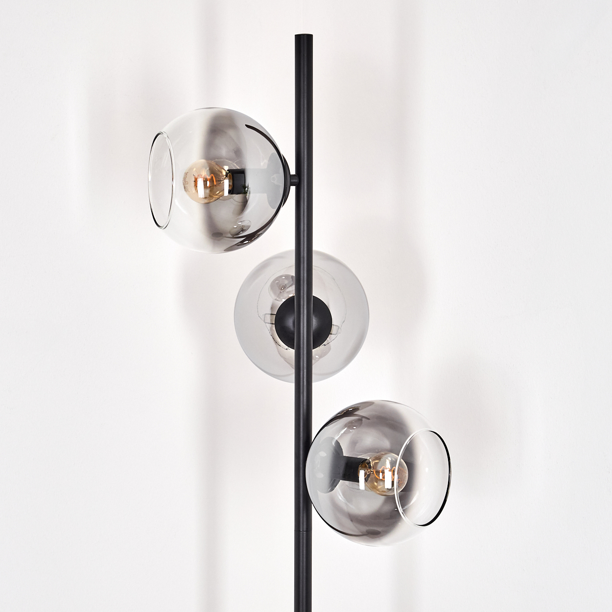 Eine moderne Stehlampe mit drei Glaskugelschirmen. Der schwarze Metallrahmen hält die Kugeln mit sichtbaren Glühbirnen.