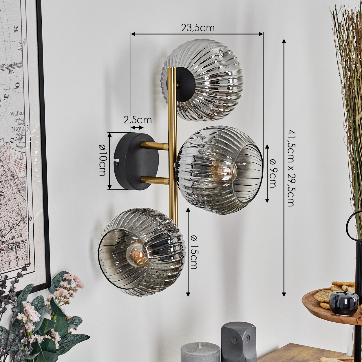 Eine Wandlampe mit drei Glaskugeln. Maße sind angegeben. Der Hintergrund umfasst eine Karte, Blumen und ein Serviertablett.