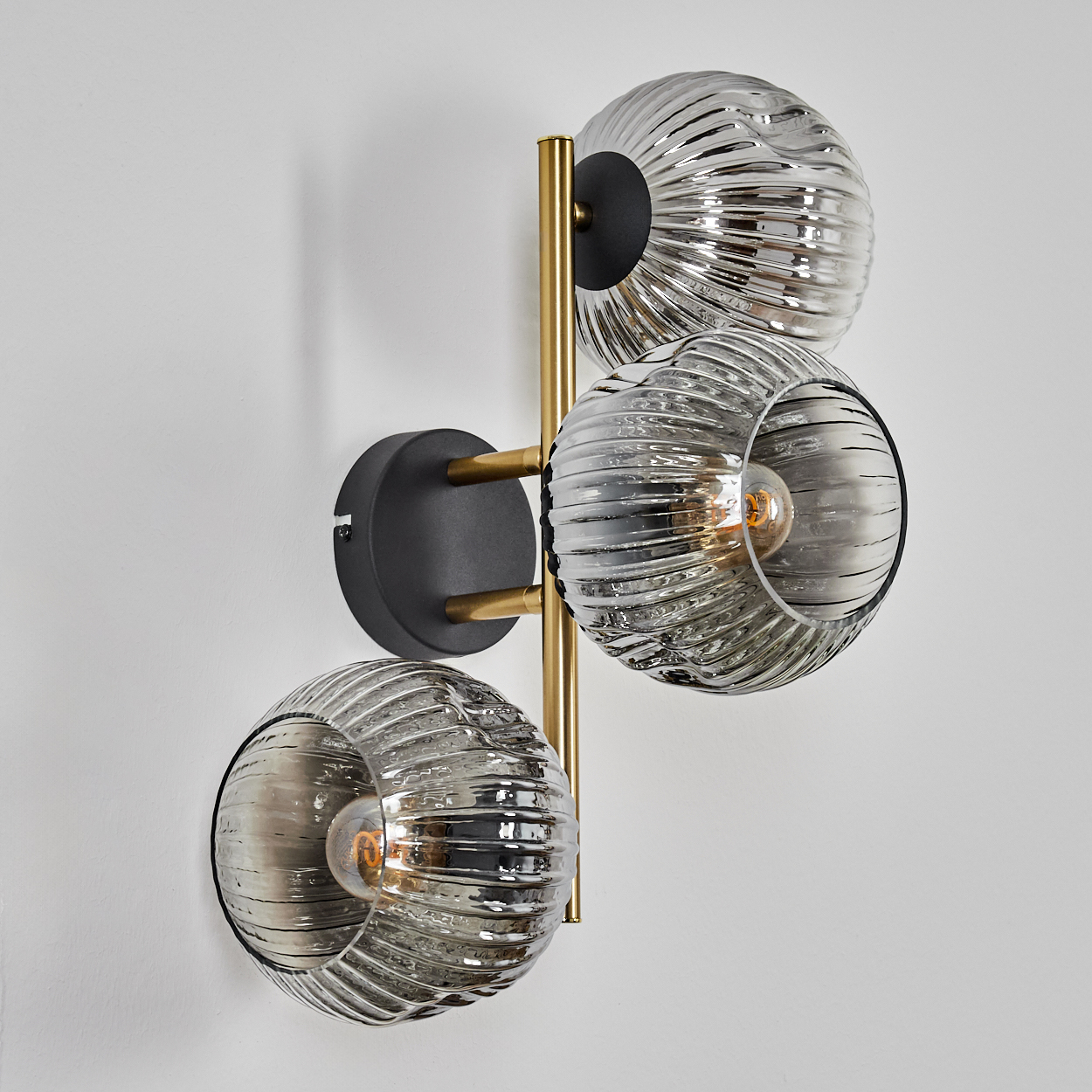 Eine moderne Wandlampe mit drei Glaskugelschirmen. Die Leuchte hat ein Messing- und schwarzes Metallgestell an einer weißen Wand.