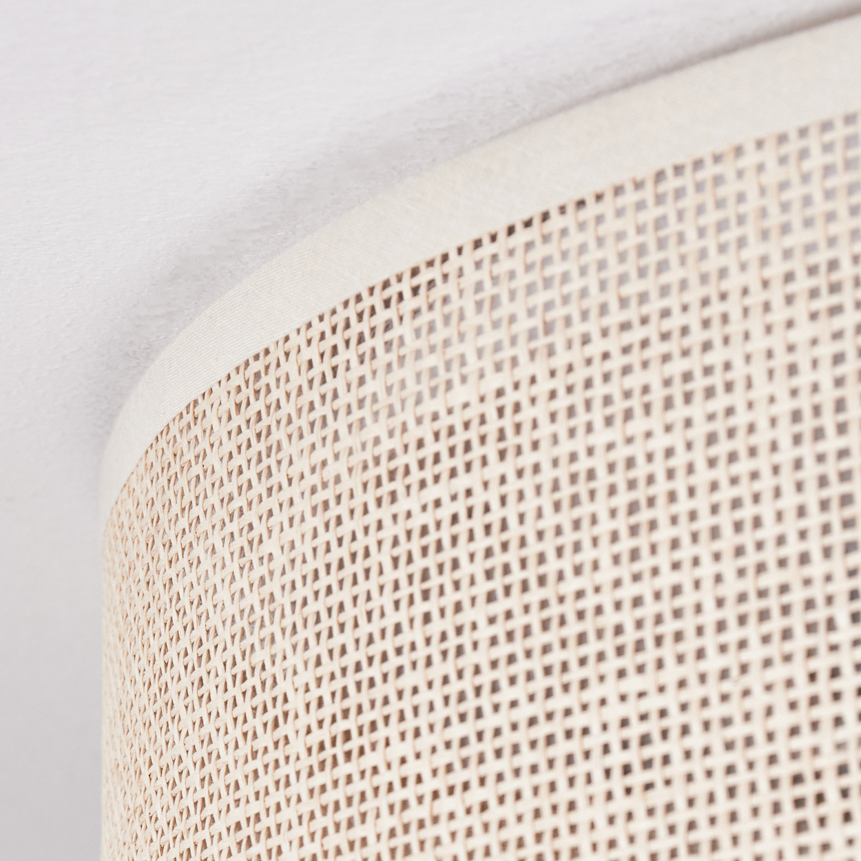 Nahaufnahme eines gewebten Lampenschirms in hellbeige. Der Hintergrund ist eine weiße Wand, das Licht ist diffus.