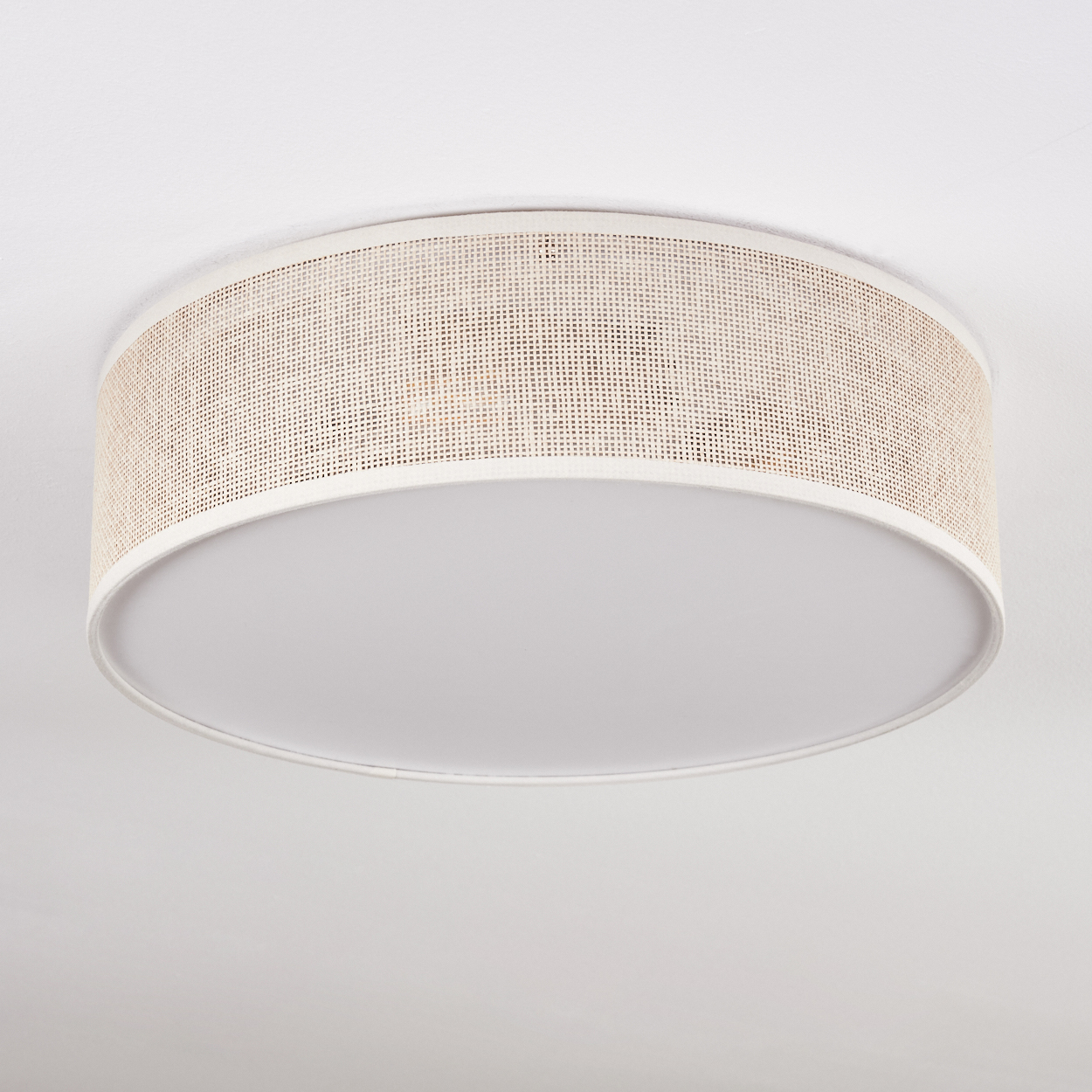 Eine runde Deckenlampe mit einem Schirm aus geflochtenem Rattan und einem weißen, abgerundeten Diffusor. Der Hintergrund ist eine weiße Decke.