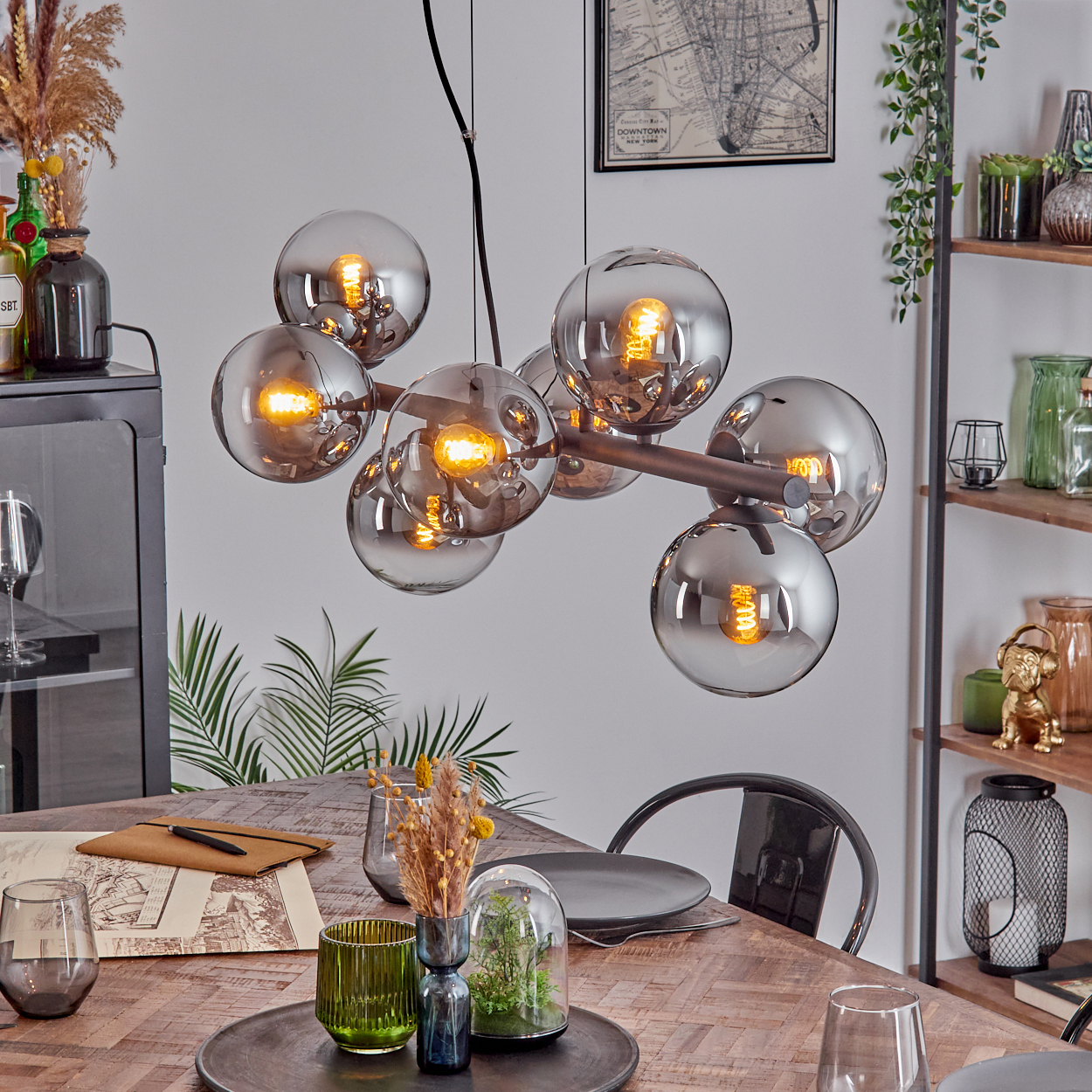 Ein modernes Esszimmer mit einem großen, kugelförmigen Kronleuchter. Ein Holztisch ist mit Dekorationsartikeln gedeckt, und eine Karte hängt an der Wand.