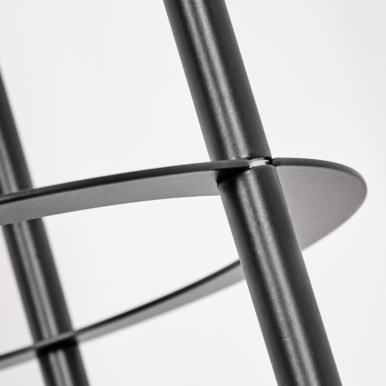 Nahaufnahme eines schwarzen Metallstuhls. Die Beine und die Sitzstütze des Stuhls sind vor einem weißen Hintergrund zu sehen. Der Fokus liegt auf der Verbindung.