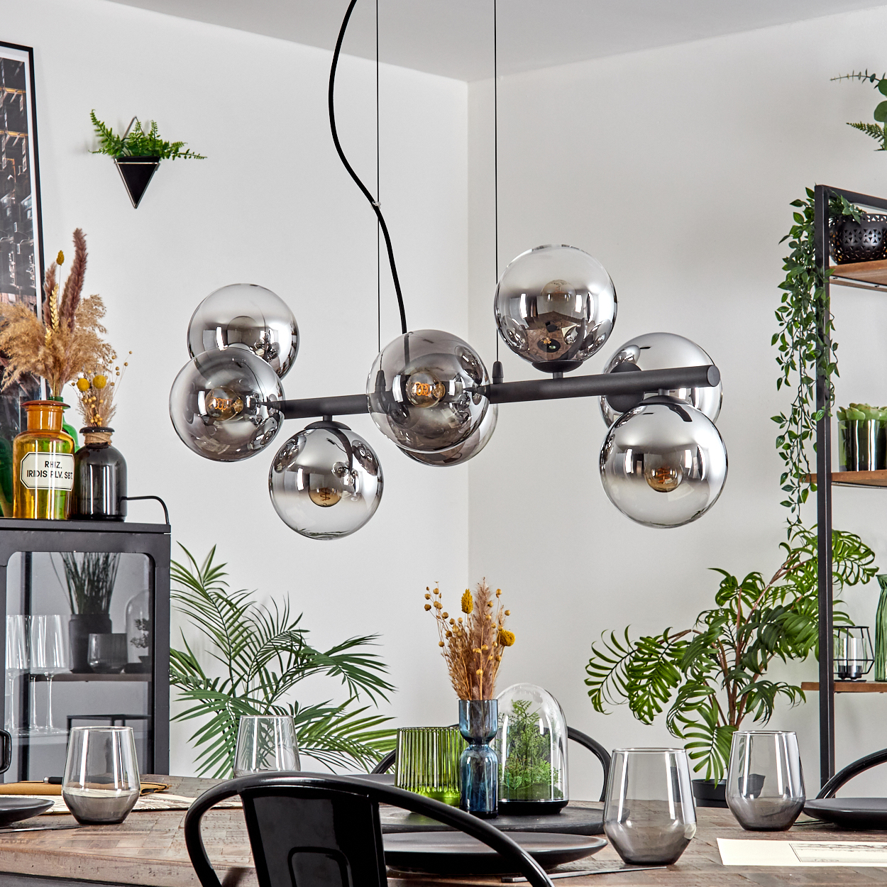 Ein Esszimmer mit einem gedeckten Tisch. Eine moderne Hängelampe hängt darüber. Pflanzen und Dekoration sind im Raum vorhanden.