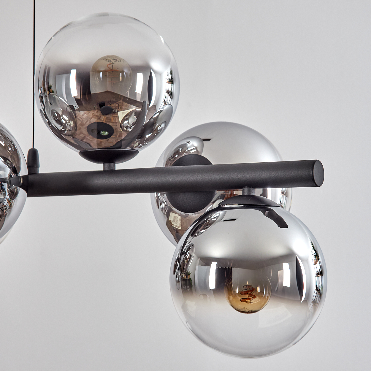 Eine moderne Deckenleuchte mit mehreren kugelförmigen Glasschirmen, die die Umgebung reflektieren. Die Leuchte hat einen schwarzen Balken und einen weißen Hintergrund.