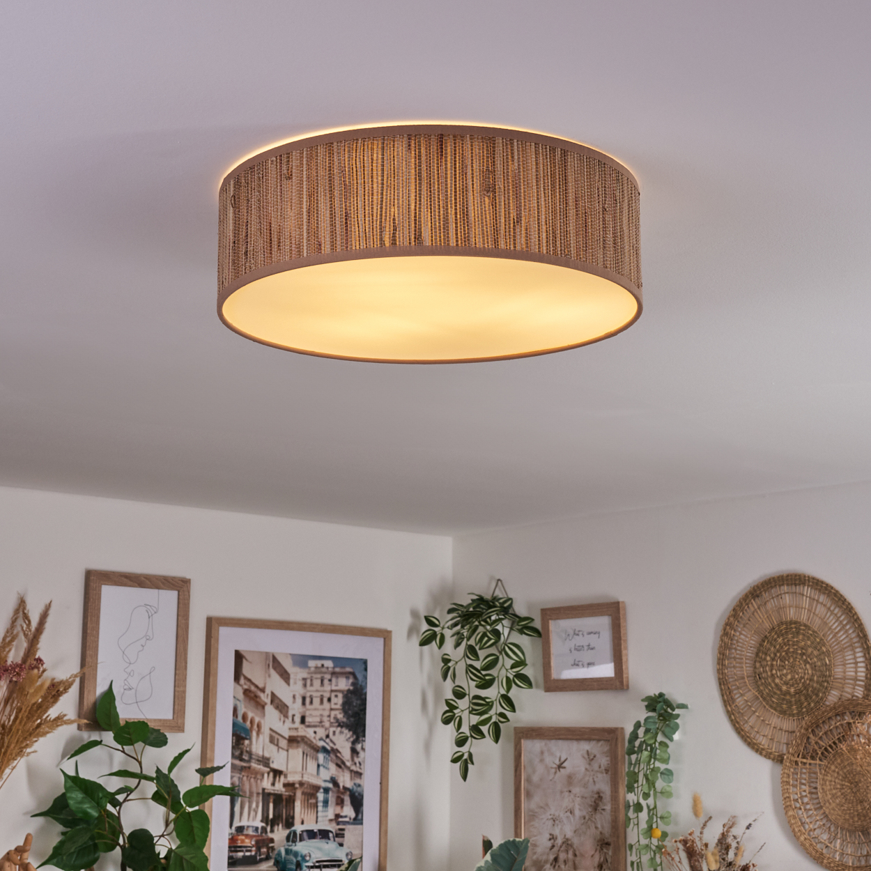 Eine runde Deckenlampe aus Weide ist der Blickfang. Darunter befinden sich gerahmte Kunst, Pflanzen und Wanddekoration. Die Wand ist weiß.