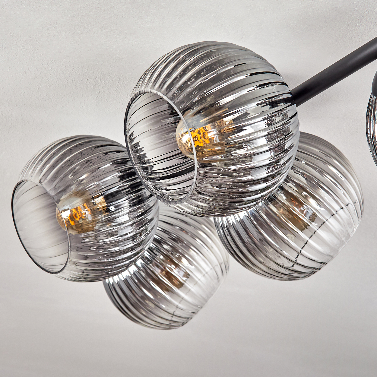 Eine moderne Deckenleuchte mit fünf kugelförmigen, geriffelten Glasschirmen. Jede Schirm hat eine warme, leuchtende Glühbirne im Inneren.