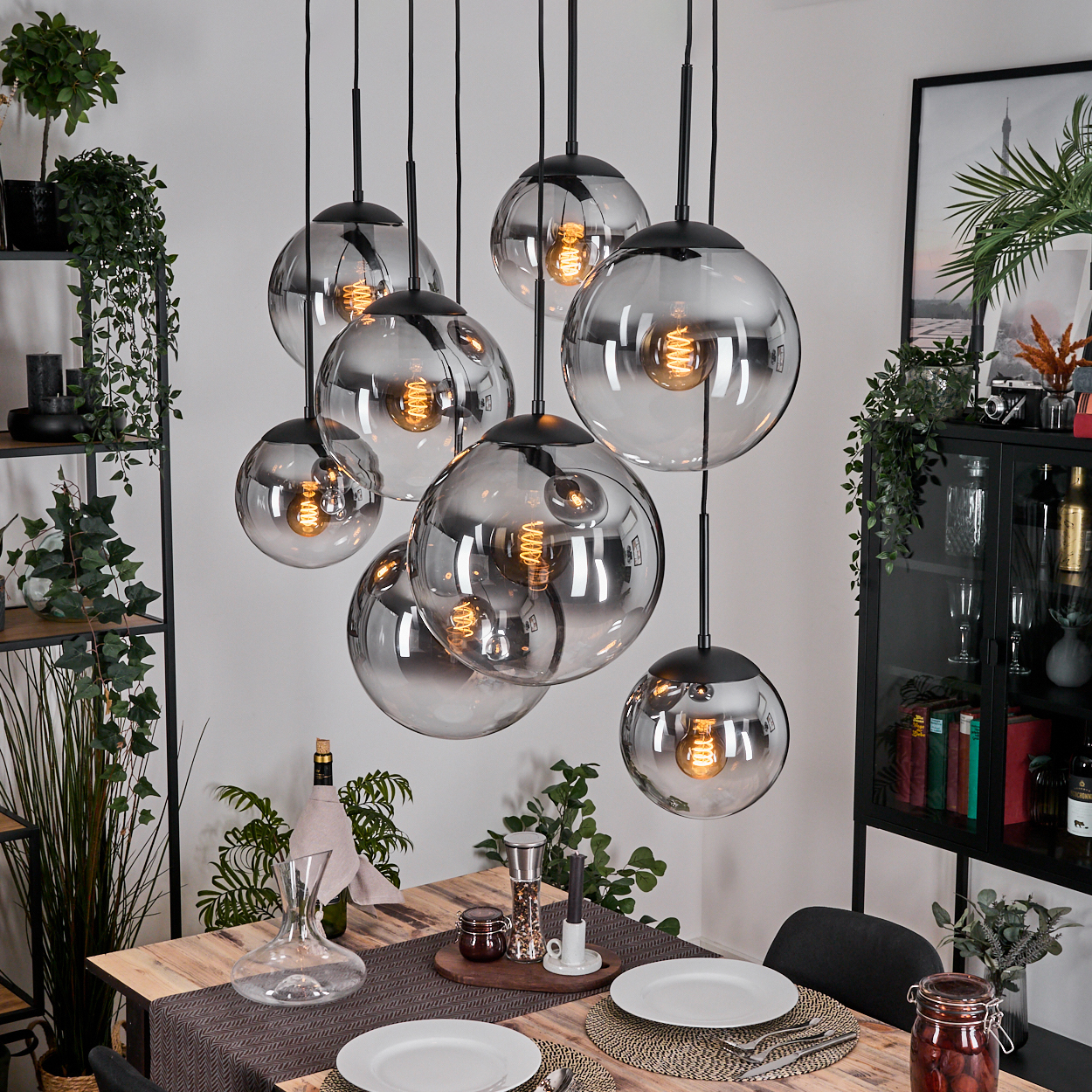 Esszimmer mit Holztisch, hängenden Kugelleuchten, Pflanzen und einem schwarzen Schrank. Der Tisch ist für das Abendessen gedeckt.
