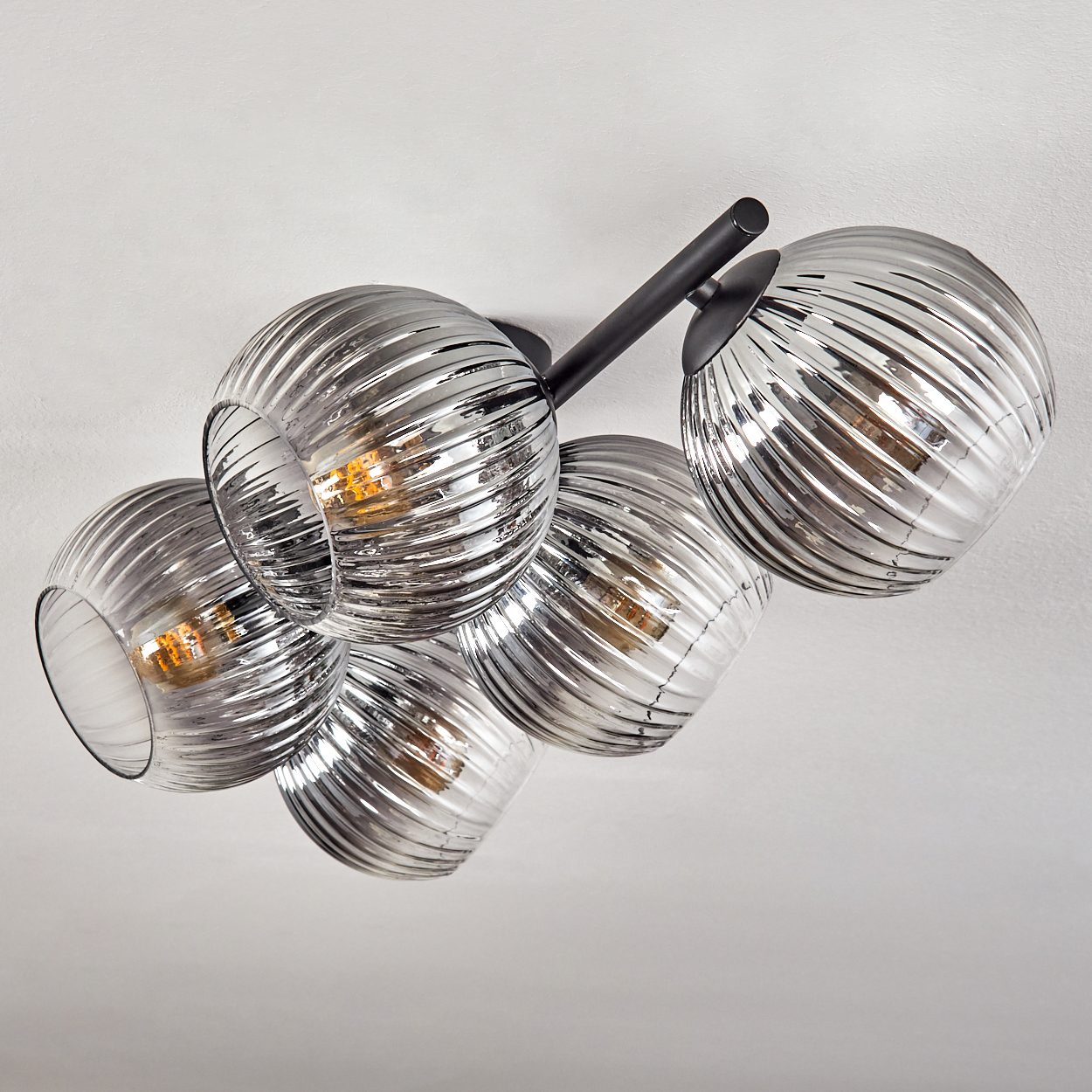 Eine moderne Deckenleuchte mit fünf kugelförmigen, silbern gefärbten Glasschirmen. Jeder Schirm hat ein Spiralmuster und die Lichter sind an.