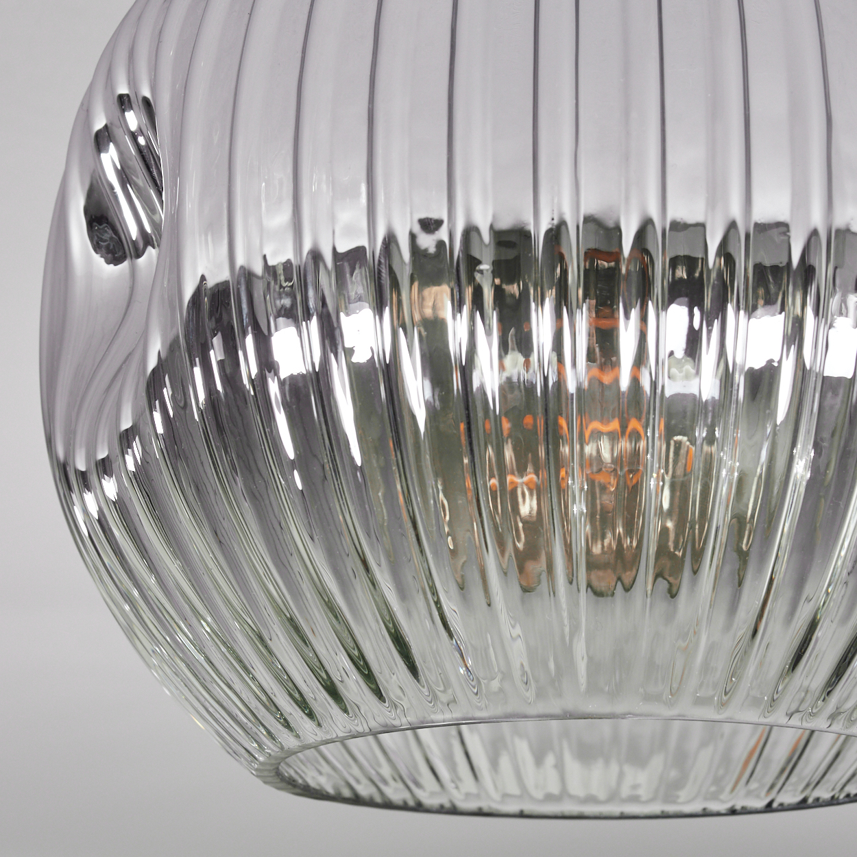 Nahaufnahme einer durchsichtigen Glasleuchte mit vertikalen Rippen. Das Glas reflektiert Licht und die Glühbirne im Inneren ist sichtbar.