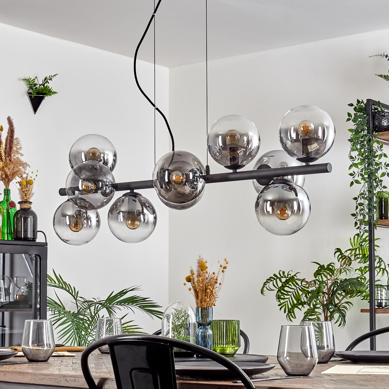 Esszimmer mit schwarzem Kronleuchter mit Glaskugeln, Holztisch, Pflanzen und Glaswaren.