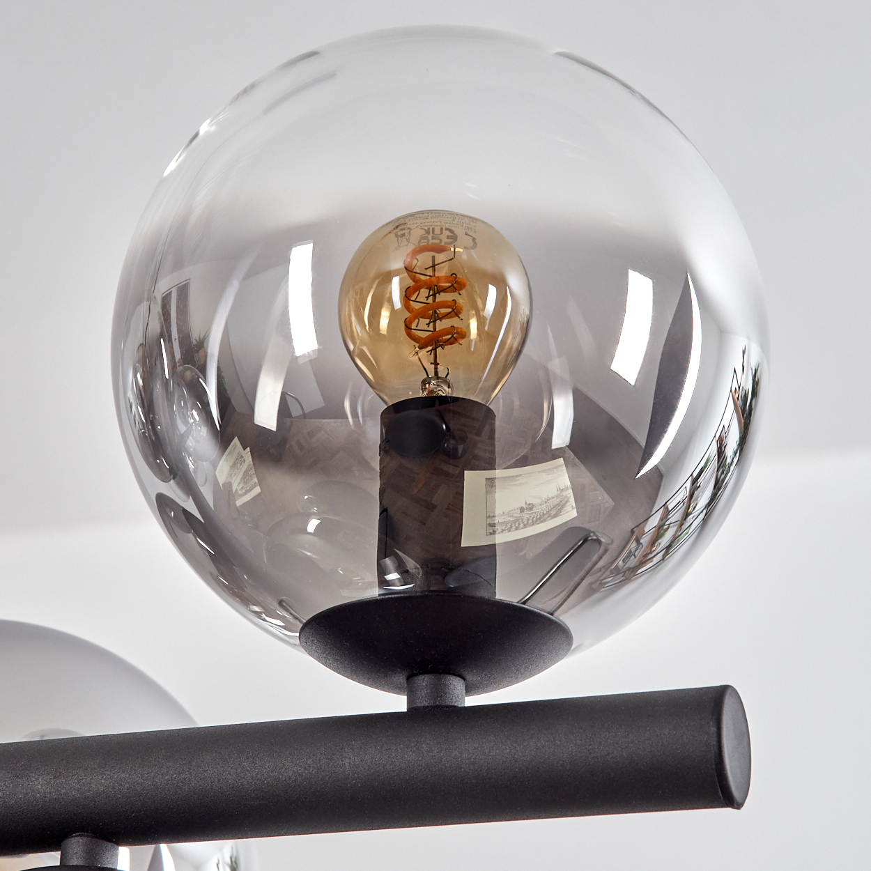 Nahaufnahme einer modernen Lampe mit transparentem Glaskugel. Eine orangefarbene Glühbirne befindet sich darin und wird von einem schwarzen Metallrahmen getragen.