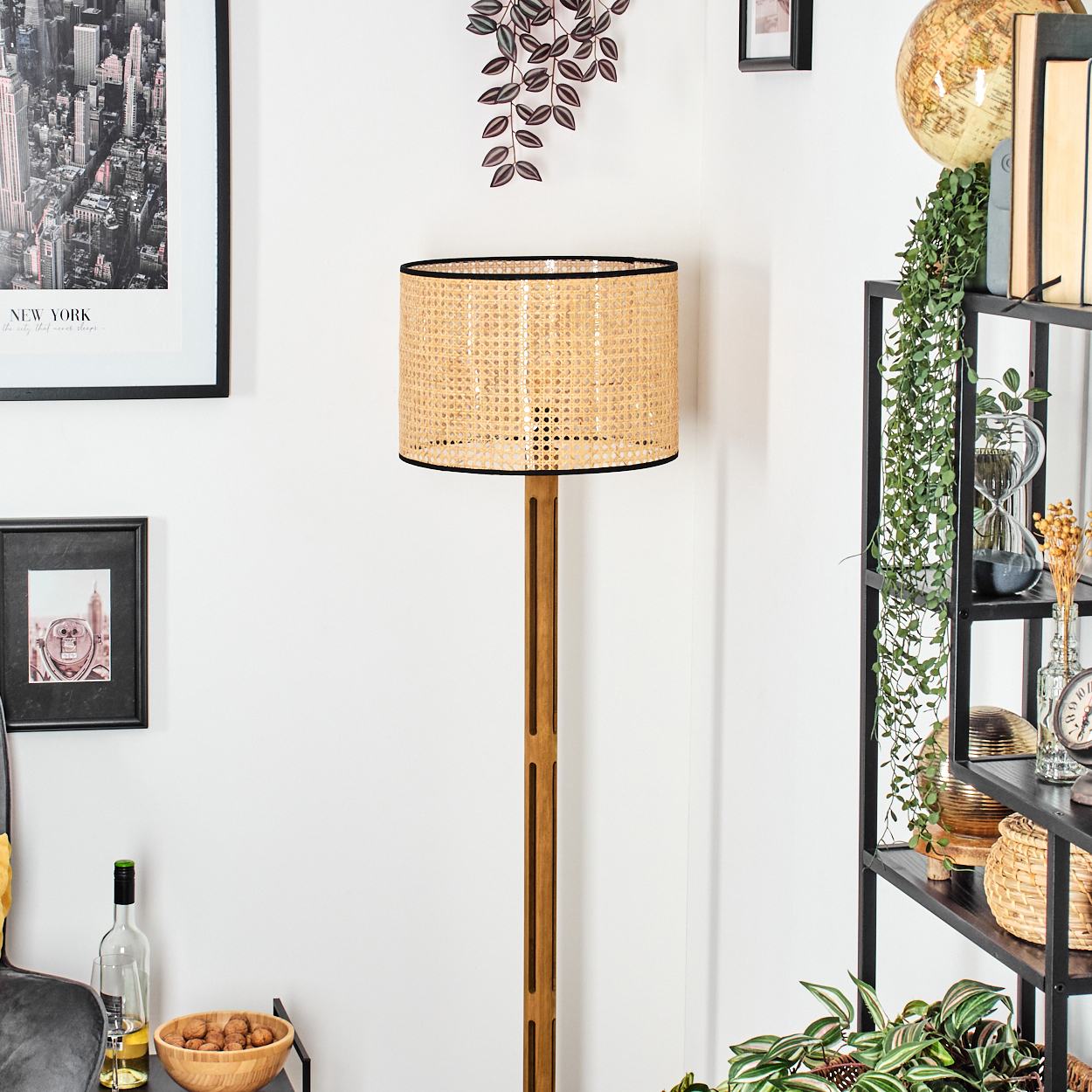 Eine Zimmerecke mit einer gewebten Lampe, Regalen und einem New York-Poster. Pflanzen und Dekorationsgegenstände sind ebenfalls sichtbar.
