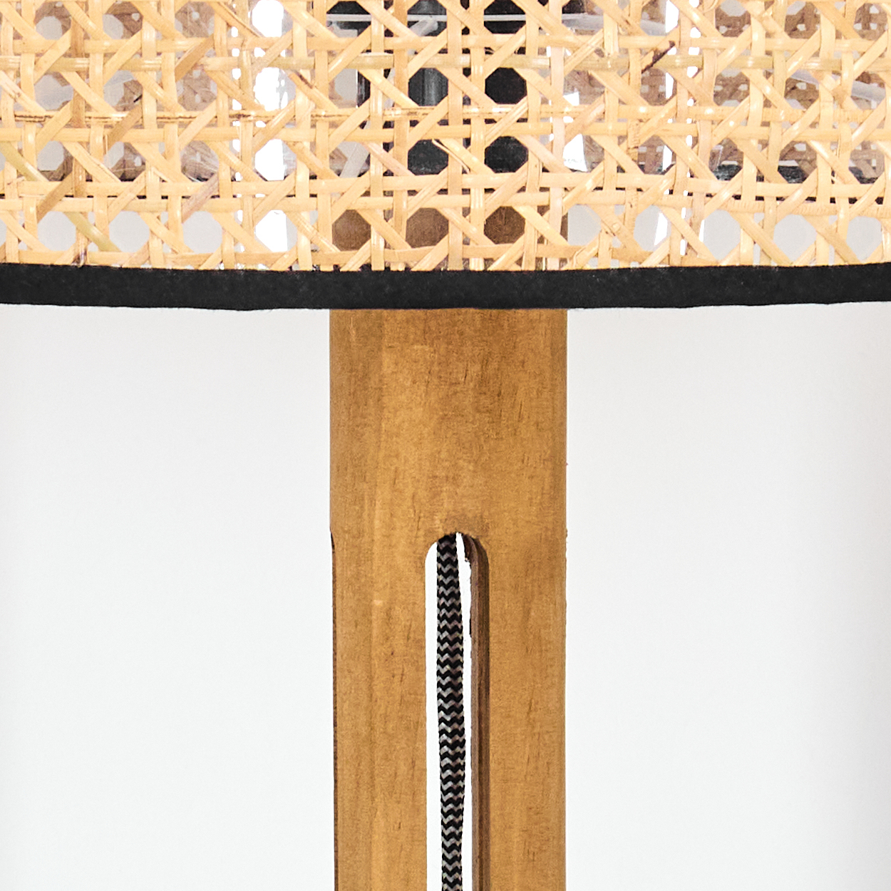 Nahaufnahme einer Lampe. Gewebter Rattan-Lampenschirm über einer Holzstütze. Ein schwarz-weißes Kabel verläuft die Stütze hinunter.