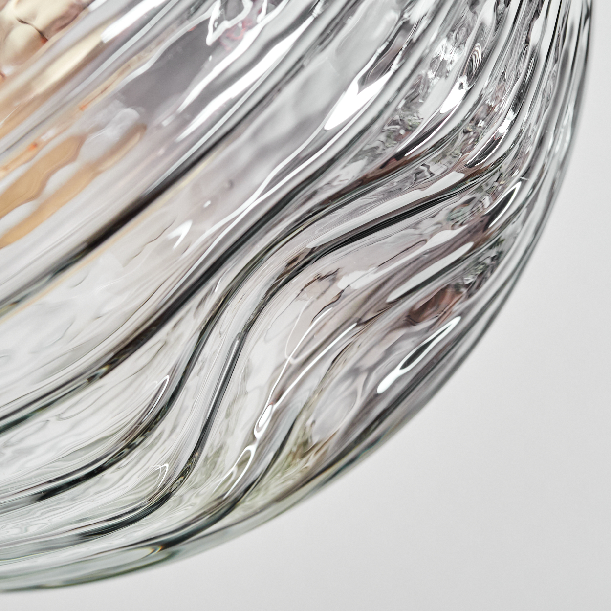 Nahaufnahme einer Glasvase mit gewellter, strukturierter Oberfläche. Licht reflektiert sich im Glas und erzeugt Streifen. Der Hintergrund ist weiß.