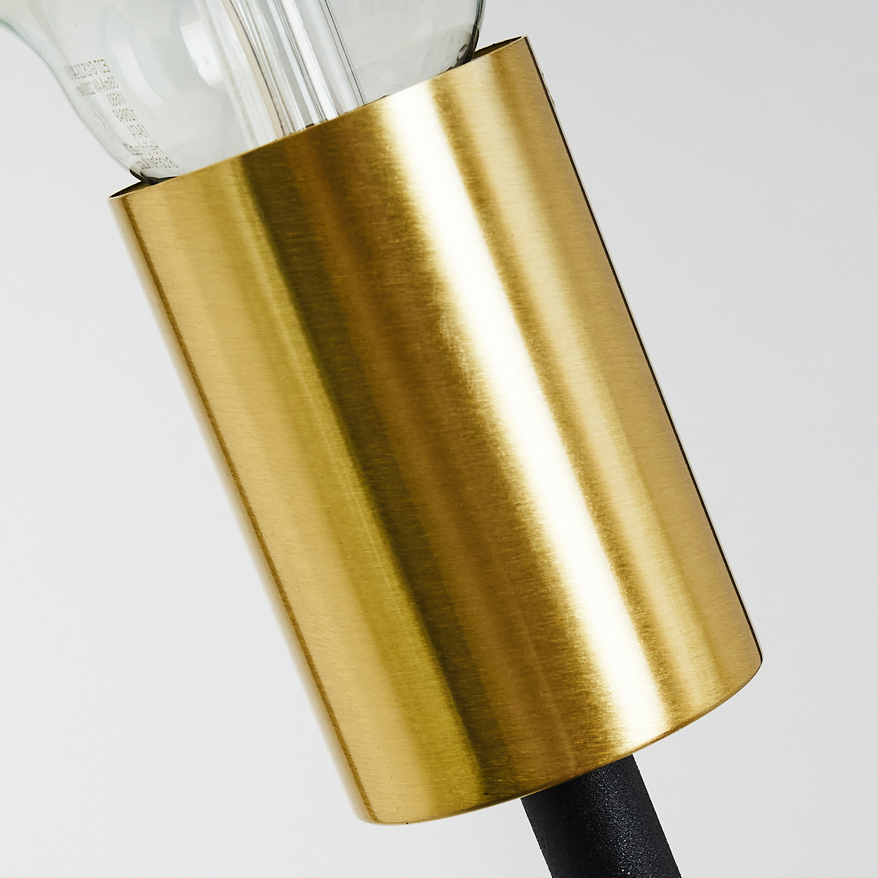 Nahaufnahme einer Lampe. Ein goldener Zylinder umgibt die Basis einer Glühbirne. Schwarzer Stiel und weißer Hintergrund.